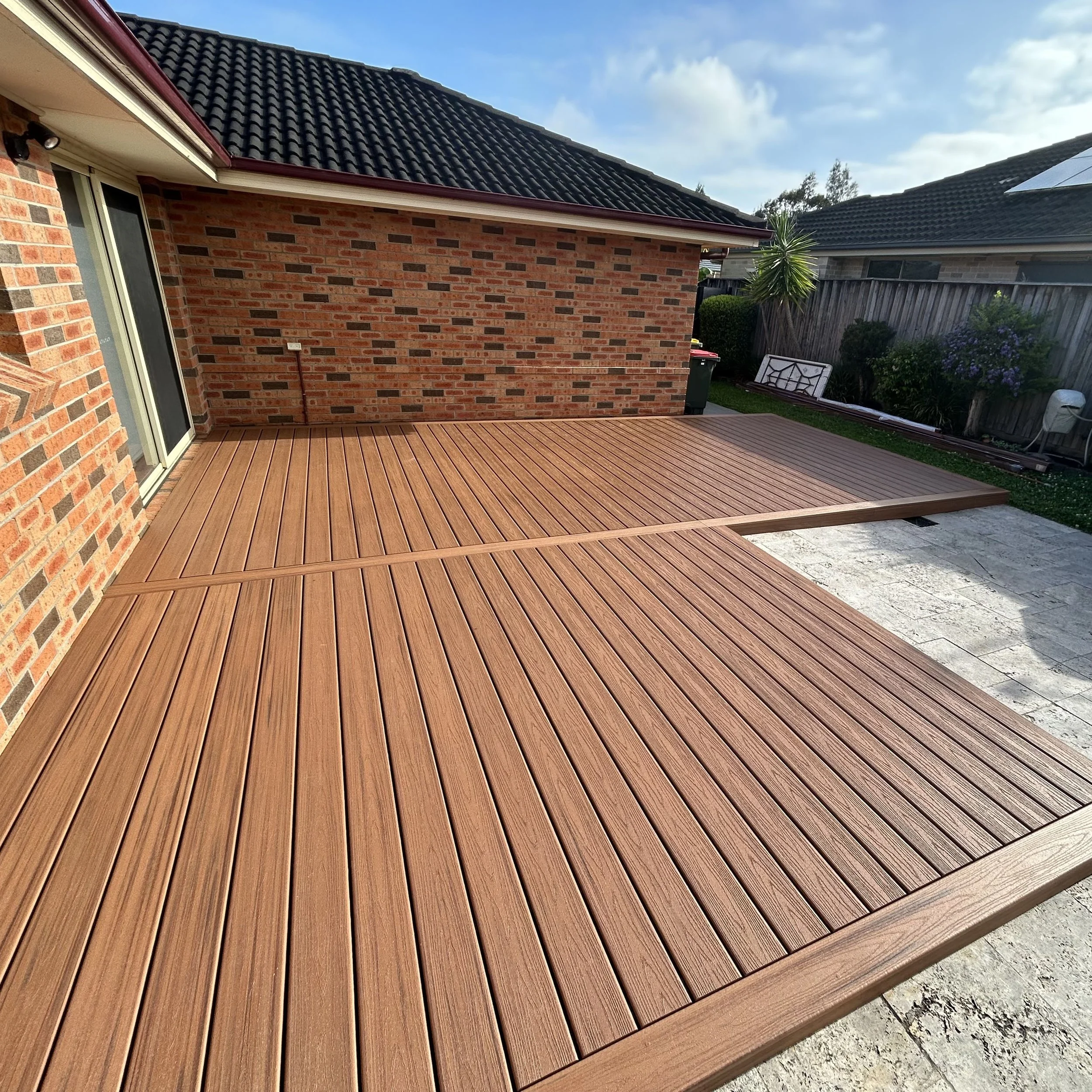 Backyard Trex deck in tiki torch beside brick home and garden outlook enhanced by Platinum Decks to create a warm, high‑end outdoor living zone