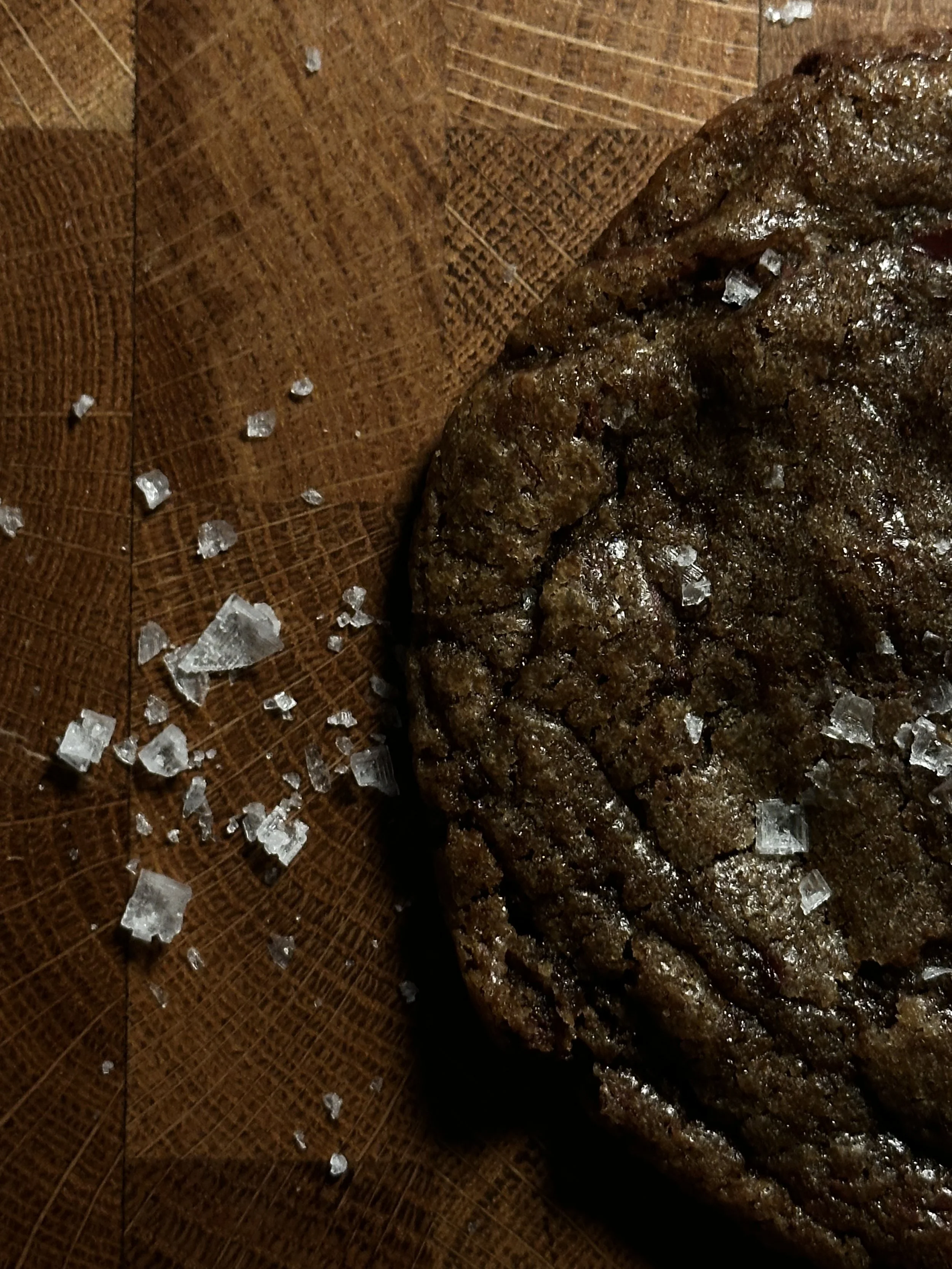 Close-up of a cooked beef patty on a wooden surface with coarse salt sprinkled on top.
