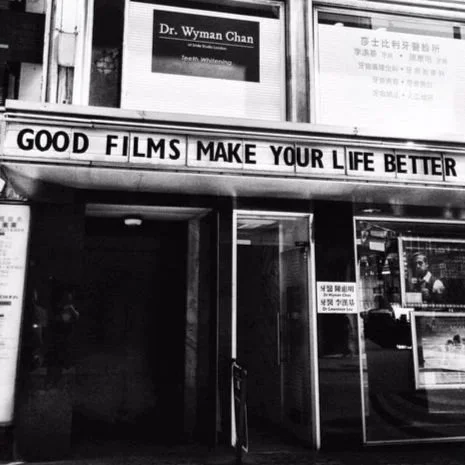 Black and white street photograph of a cinema marquee reading 'Good Films Make Your Life Better.