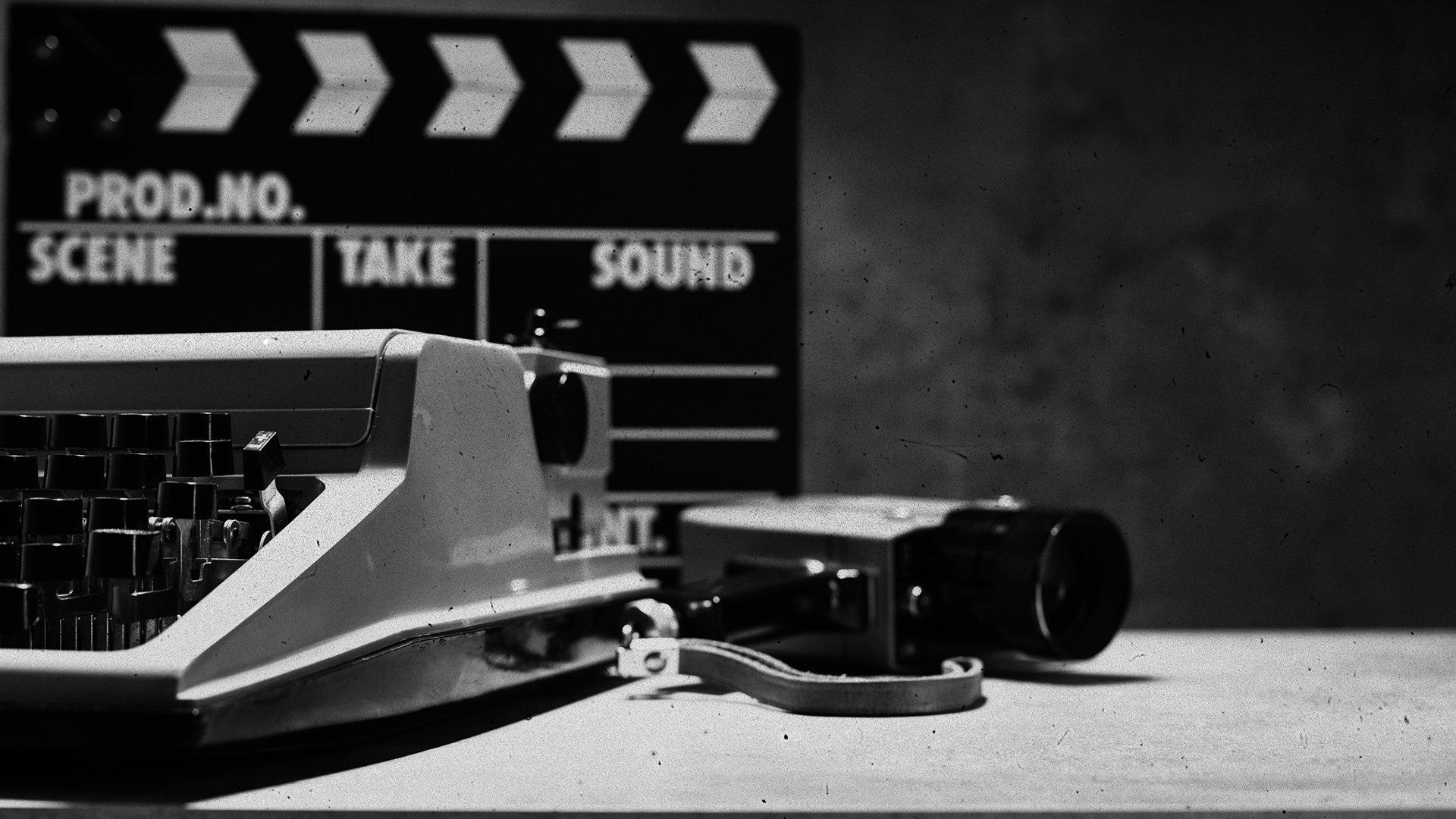 Black and white close-up of a film clapperboard, vintage typewriter, and handheld camera on a table — representing the craft of independent filmmaking and storytelling.