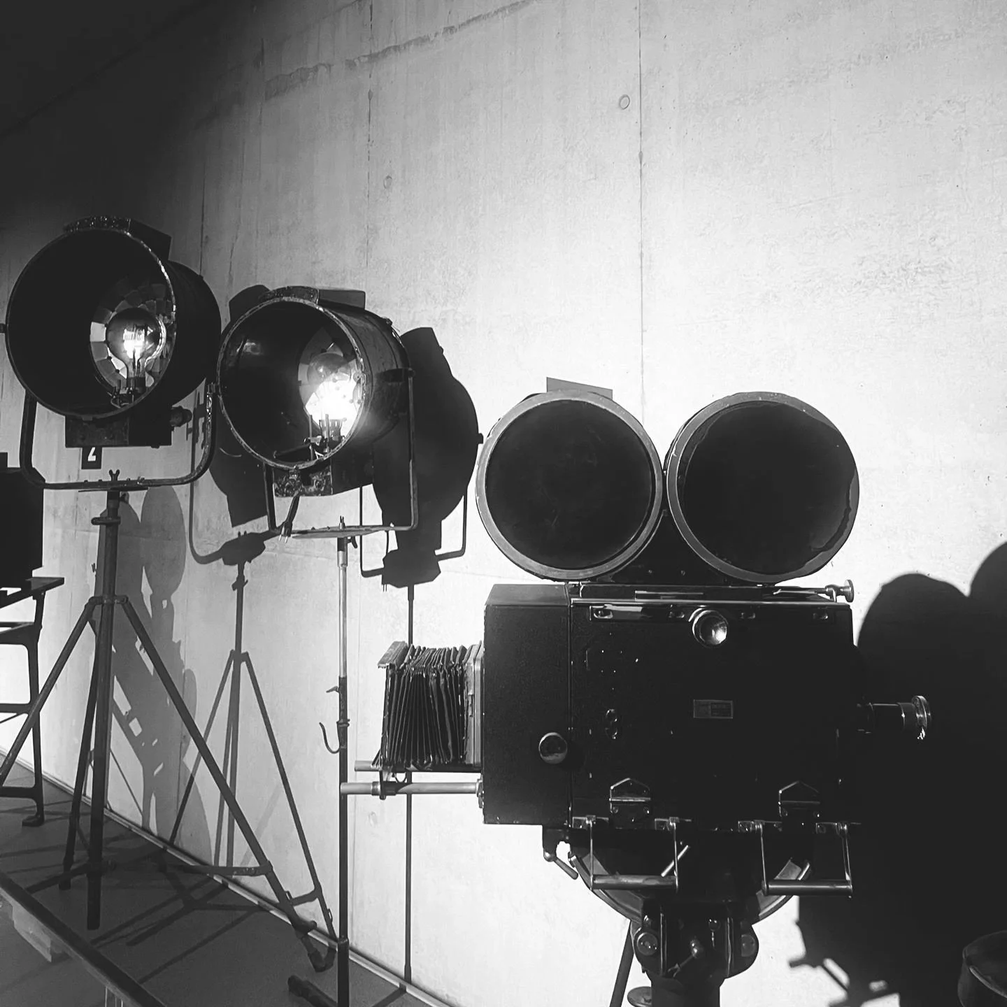 Black and white photograph of vintage film production equipment — studio lights and a classic movie camera on set.