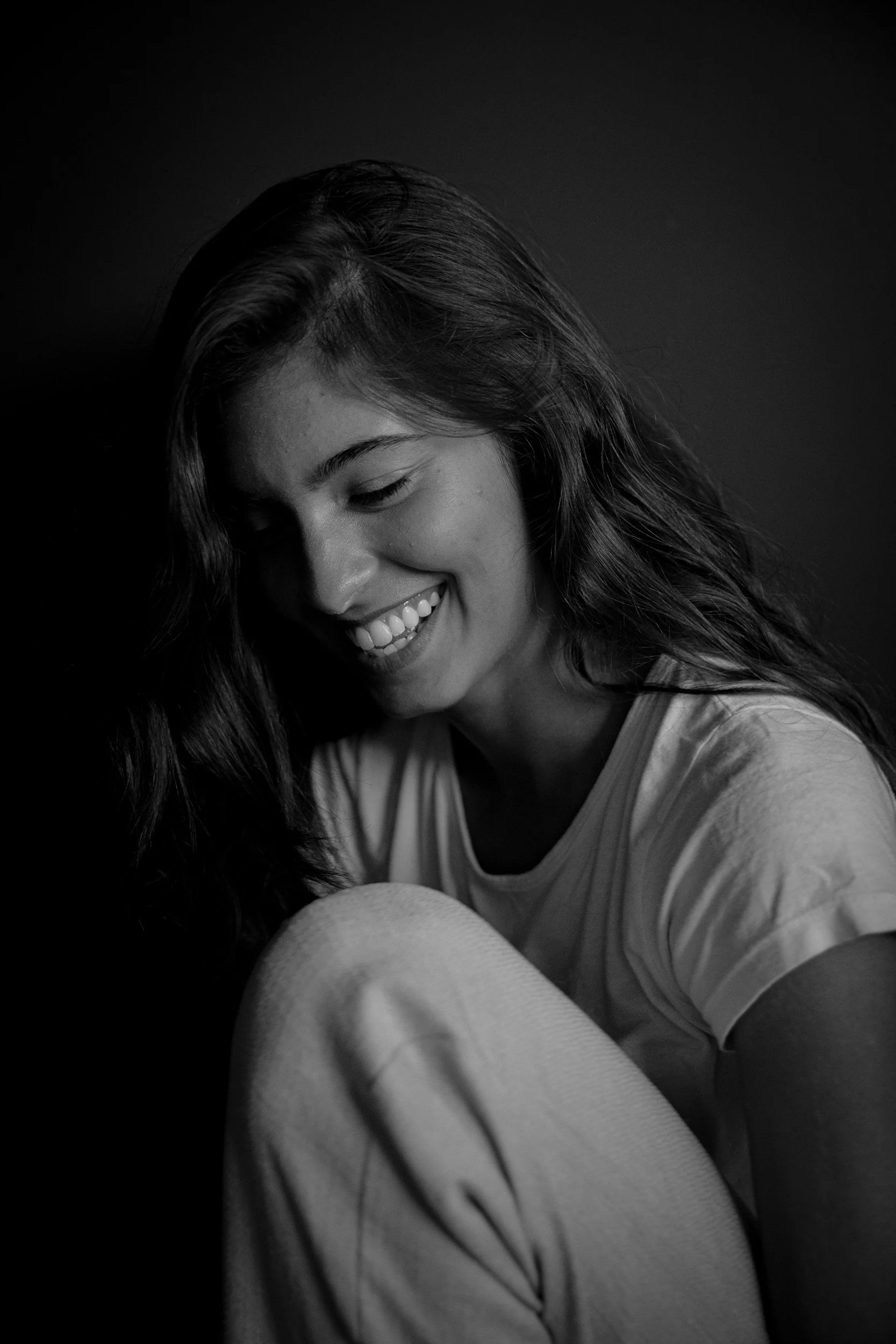 A woman smiling with her eyes closed, long dark hair, wearing a striped shirt, in black and white.