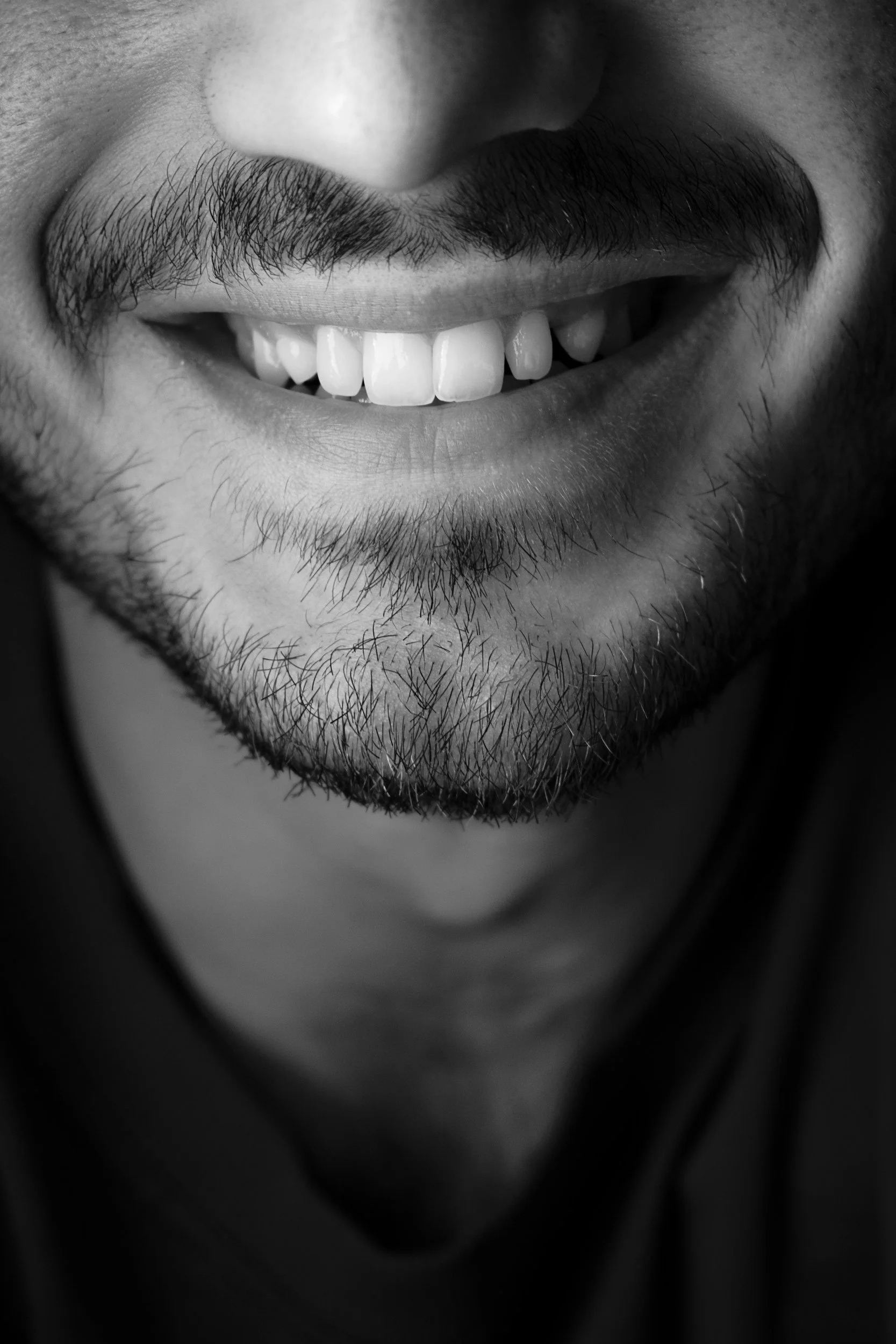 Close-up black and white photo of a person smiling, showing teeth and facial hair.