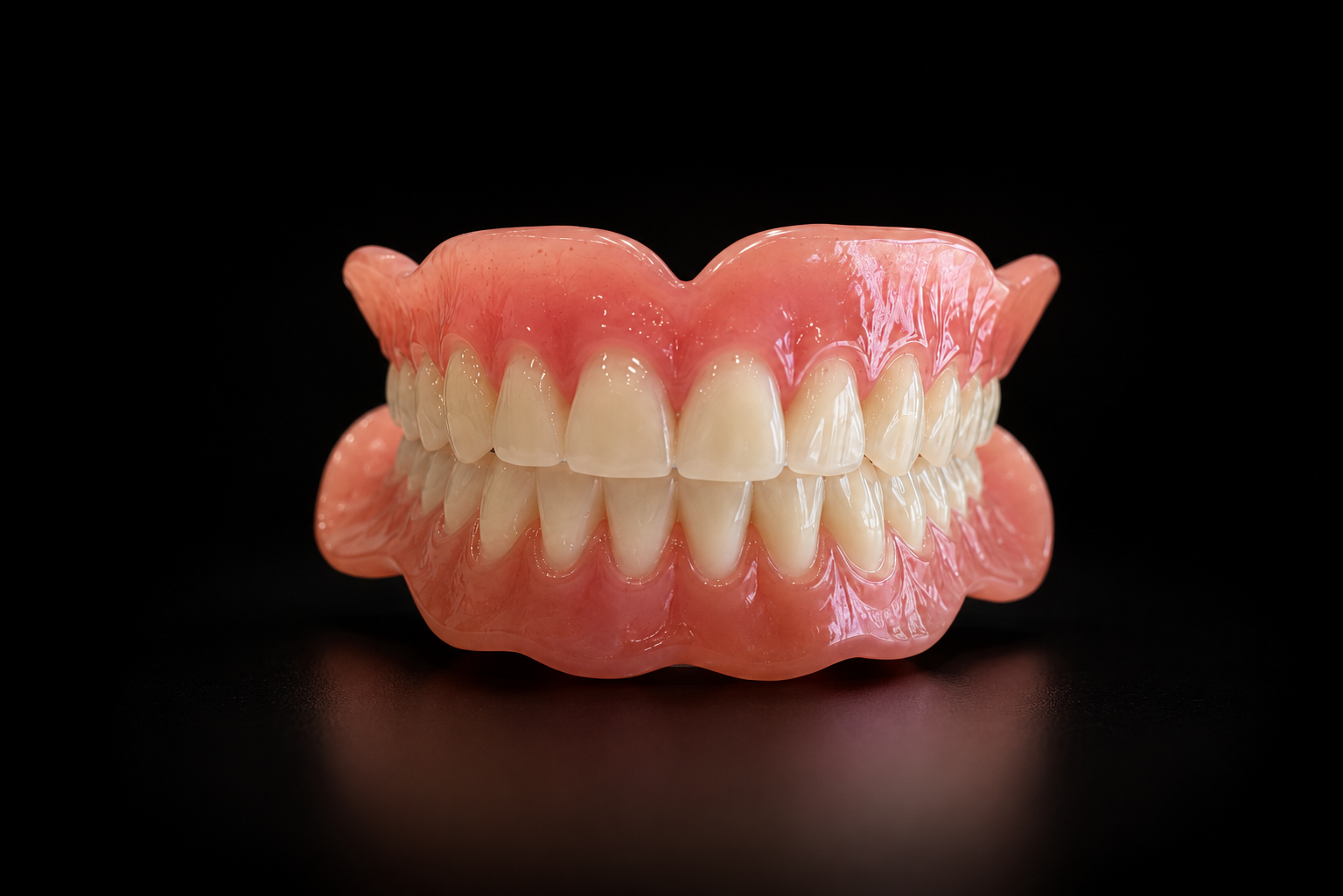 A set of artificial dentures with acrylic pink gums and realistic-looking teeth, set against a black background.