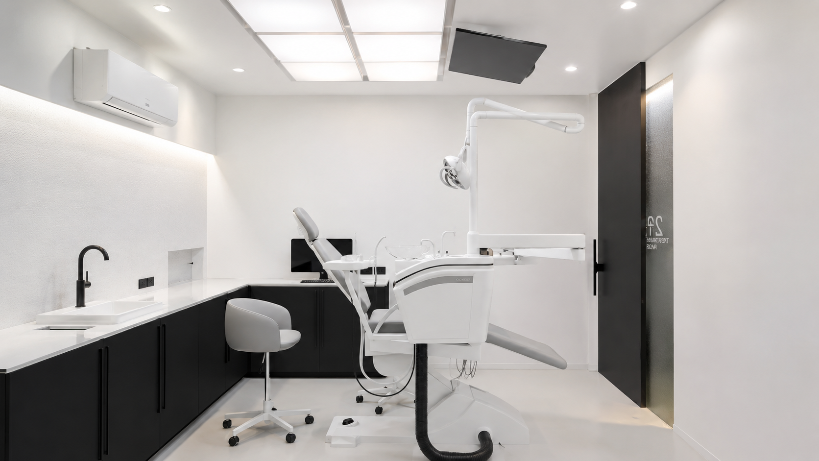 A modern dental office with a dental chair, overhead light, and monitors. The room is minimalistic with black cabinets, white walls, and equipment.