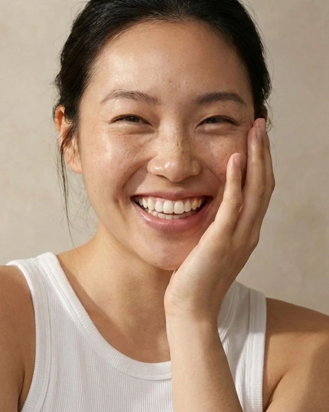Close-up of a woman with a bright smile, touching her cheek with her hand.
