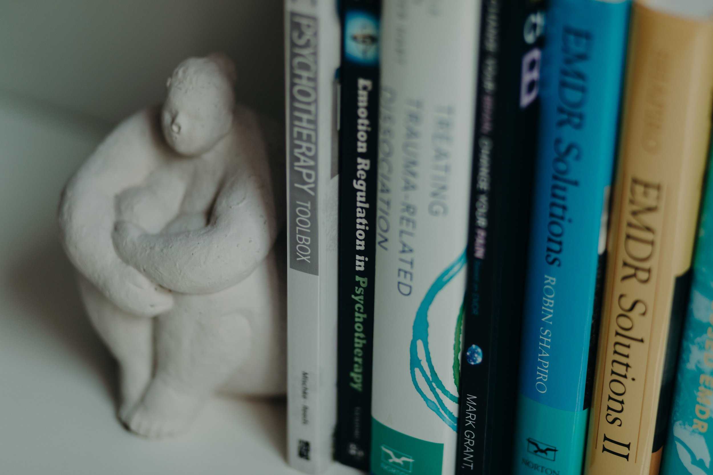 A white ceramic sculpture of a seated figure next to a row of books with various titles and colors.