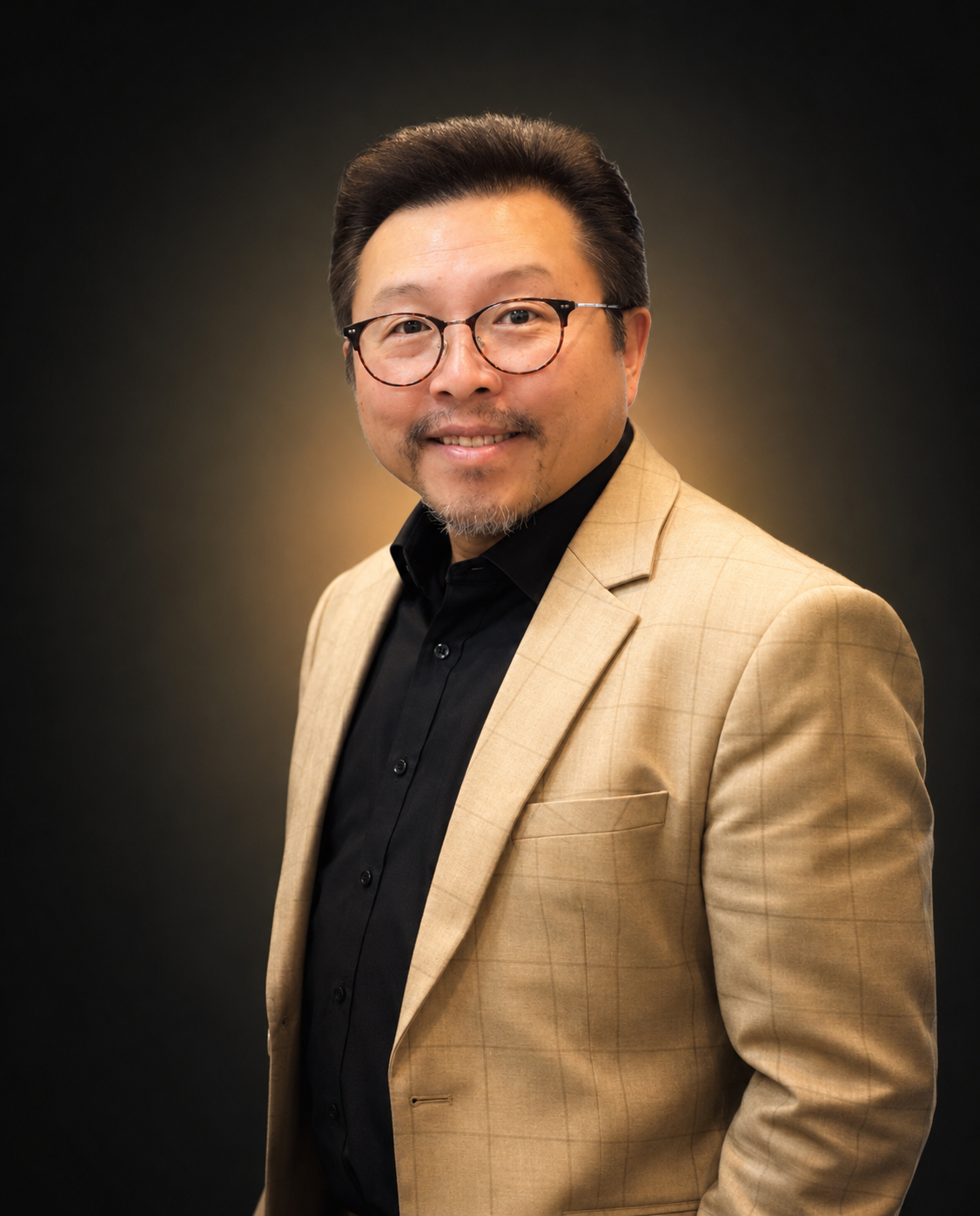 Headshot of a man wearing glasses, a black shirt, and a beige blazer against a dark gradient background.