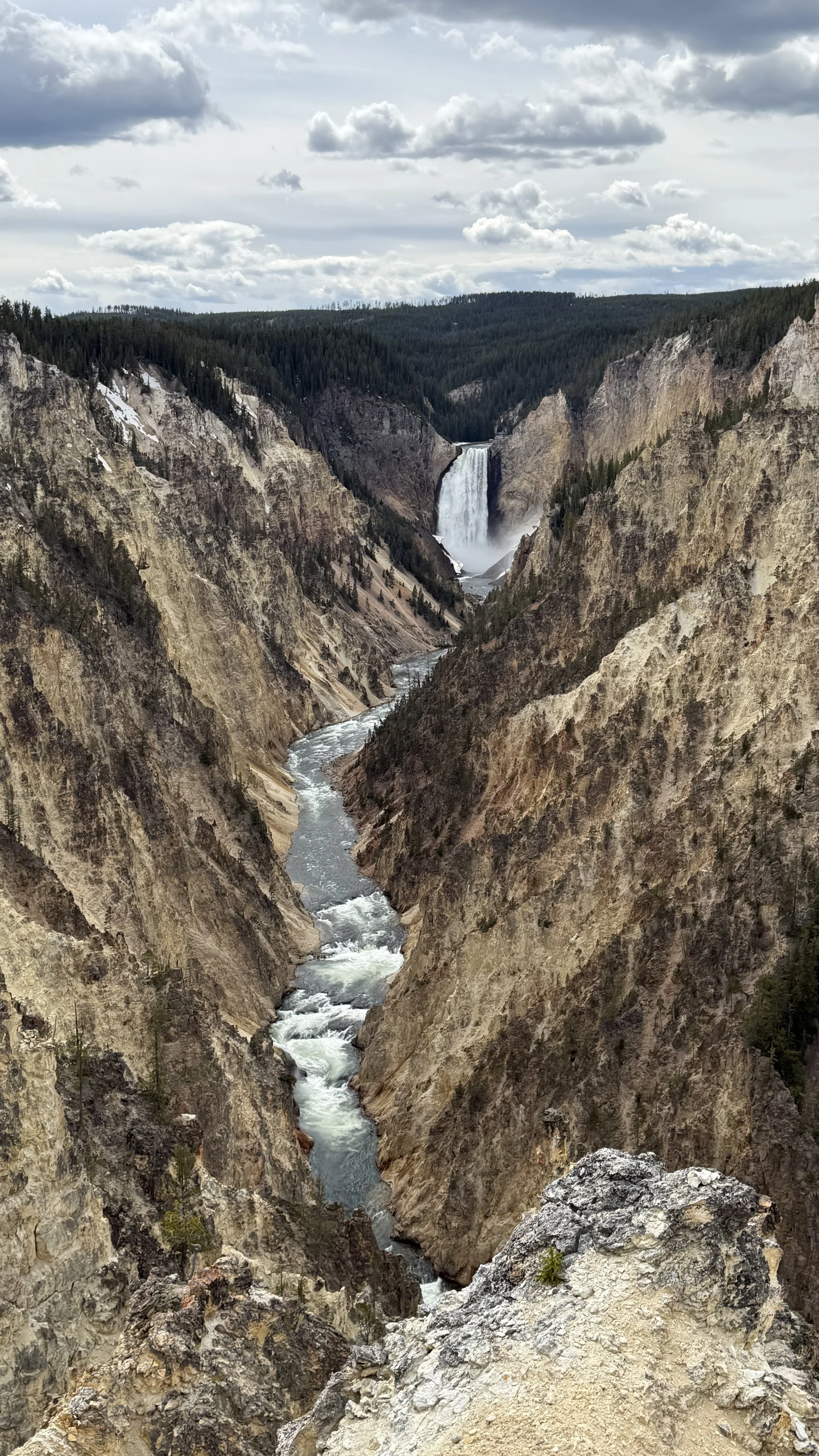 A view of Grand Canyon with a river flowing through the canyon and a waterfall in the background, with mountains and cloudy sky.
