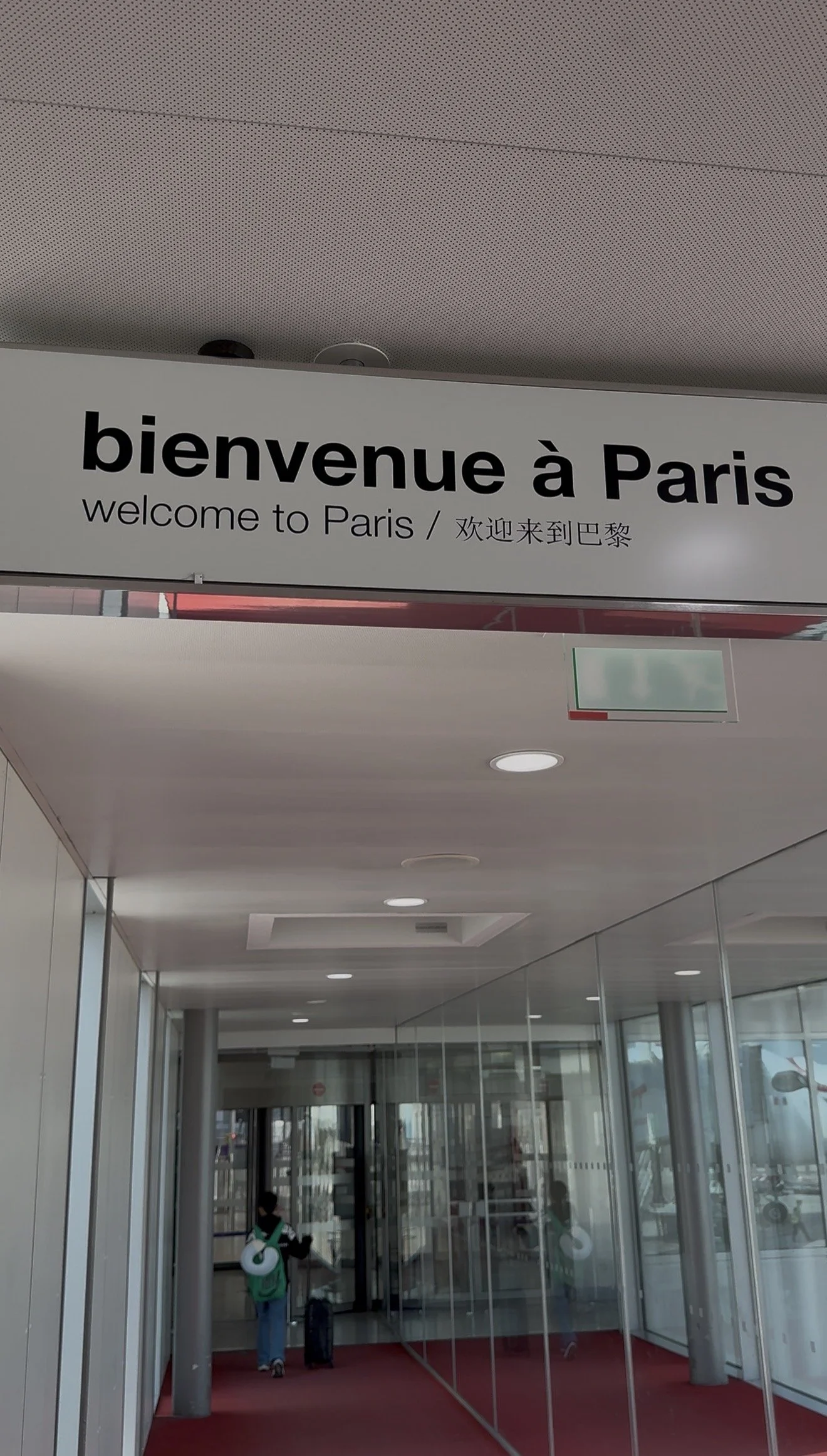 Sign welcoming travelers to Paris written in French, English, and Chinese at an airport entrance.