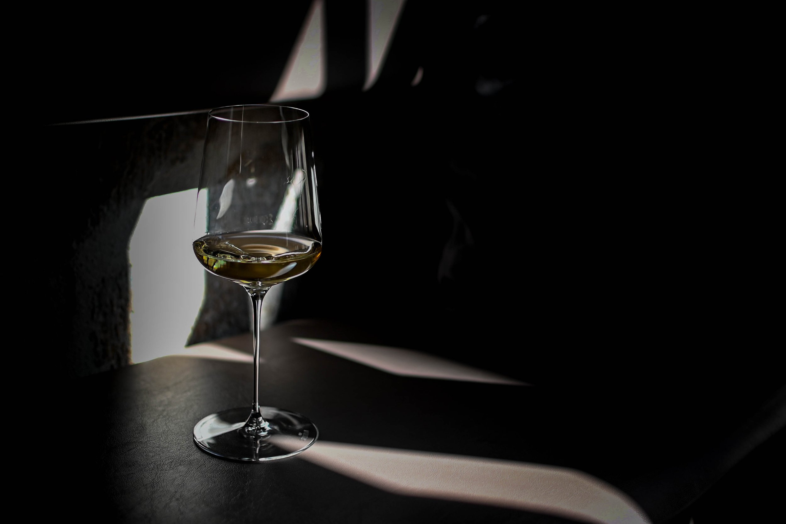 Verre à vin blanc semi-rempli, placé sur une surface noire, avec un fond sombre et une lumière réfléchie.