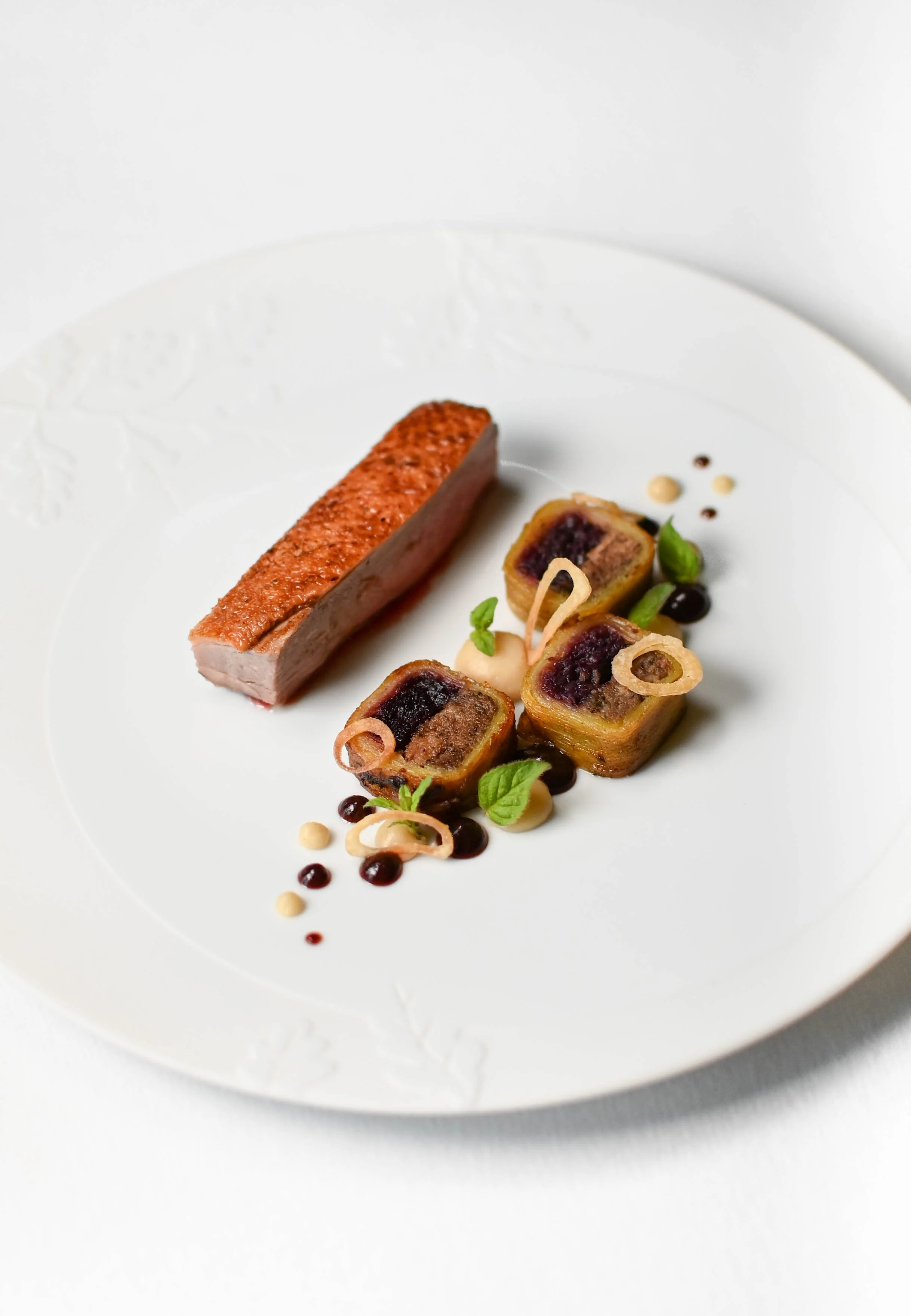 Assiette avec un filet de viande cuite, un rouleau feuilleté farci et garnitures décoratives.