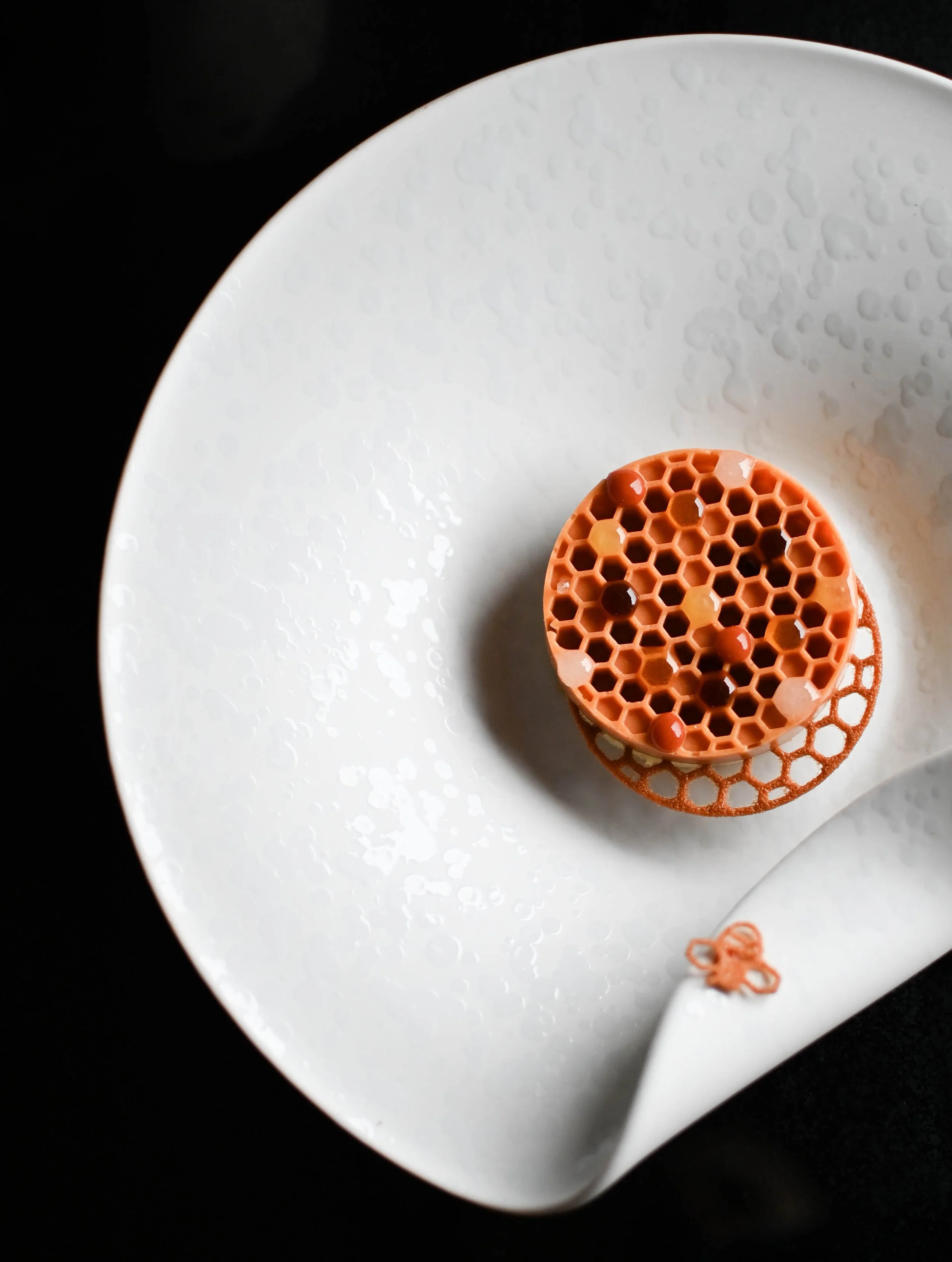 Vue partielle d'une assiette blanche avec un dessert autour du miel, placé au centre, sur fond noir.