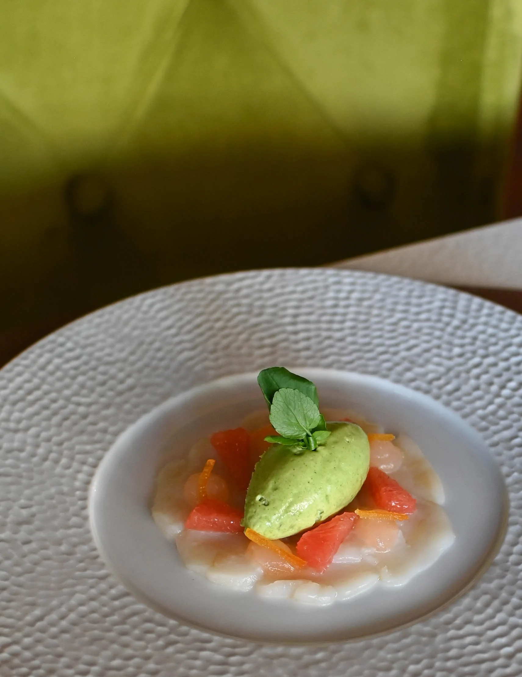 Soupe de poisson avec une crème verte, des morceaux de poisson, des carottes, et une branche de menthe