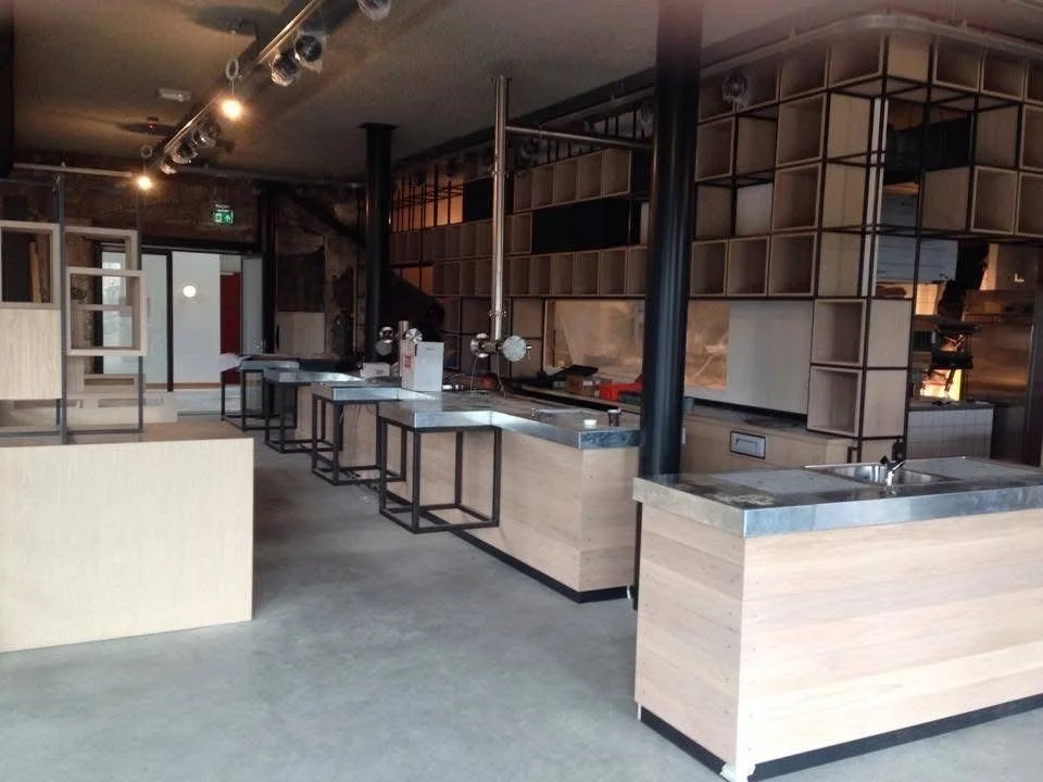 Interieur van een moderne keuken of café met houten kasten, werkbladen, en een decoratieve open plankwand, klaar voor gebruik.