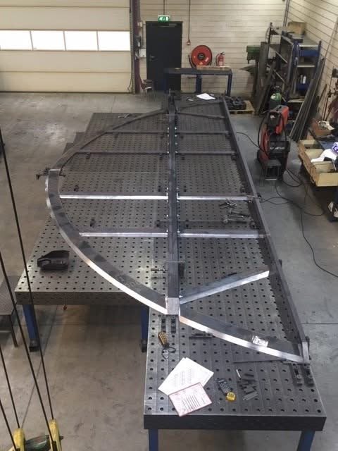 Metaalconstructie op werkbank in werkplaats met gereedschap en documenten.