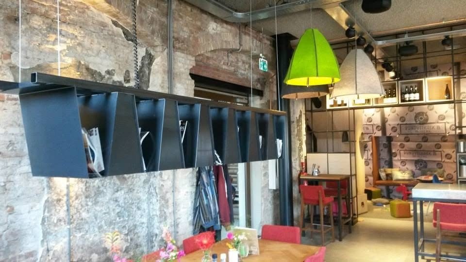 Interieur van een gezellige koffiebar met hanglampen, een muur met decoratief behang, en zitplaatsen met stoelen en banken.