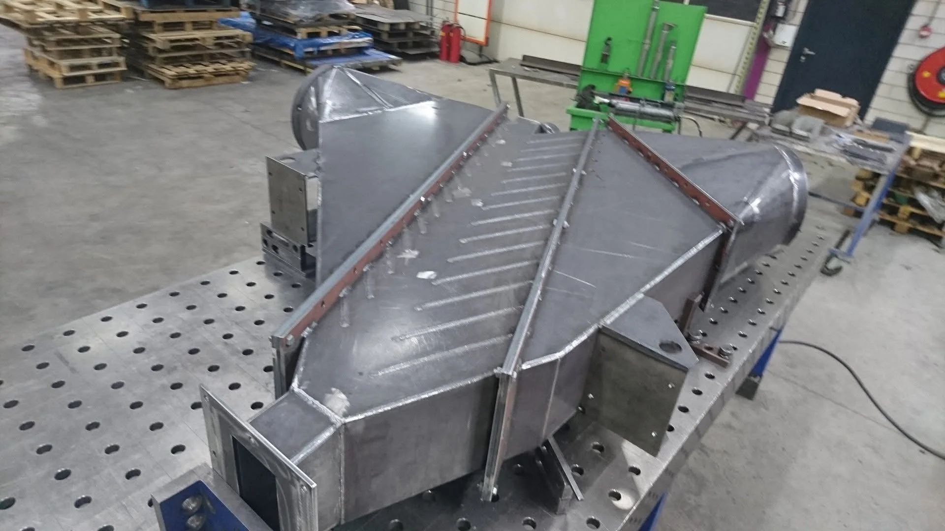 Metaalconstructie of een machineonderdeel in een werkplaats met werkbank en gereedschap op achtergrond.