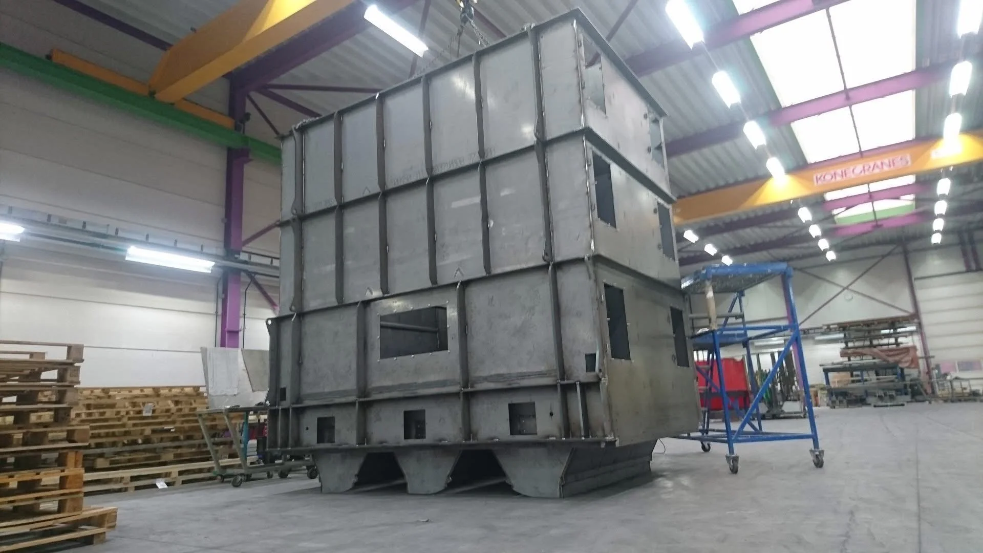 Grote metalen structuur op een ladewagen binnen een fabriekshal.