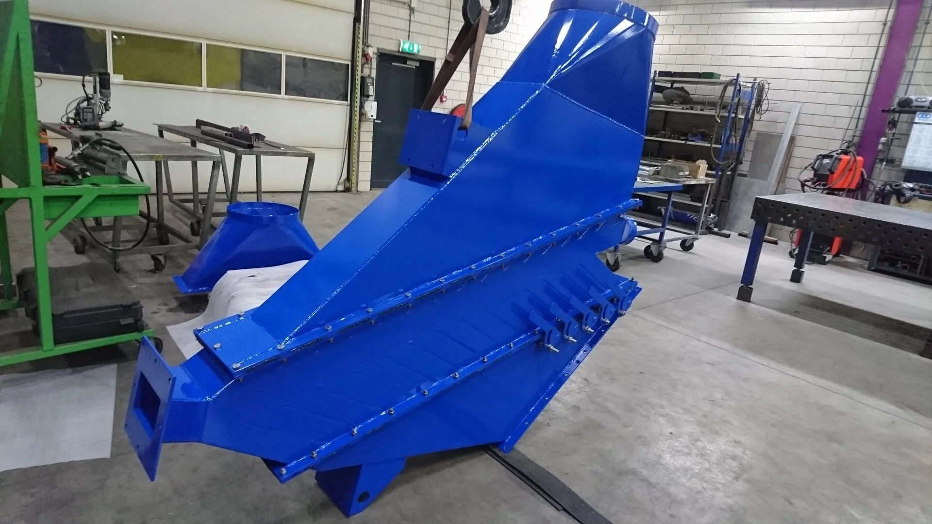 Grote blauwe industriële machine in een werkplaats met gereedschap en werkstations.