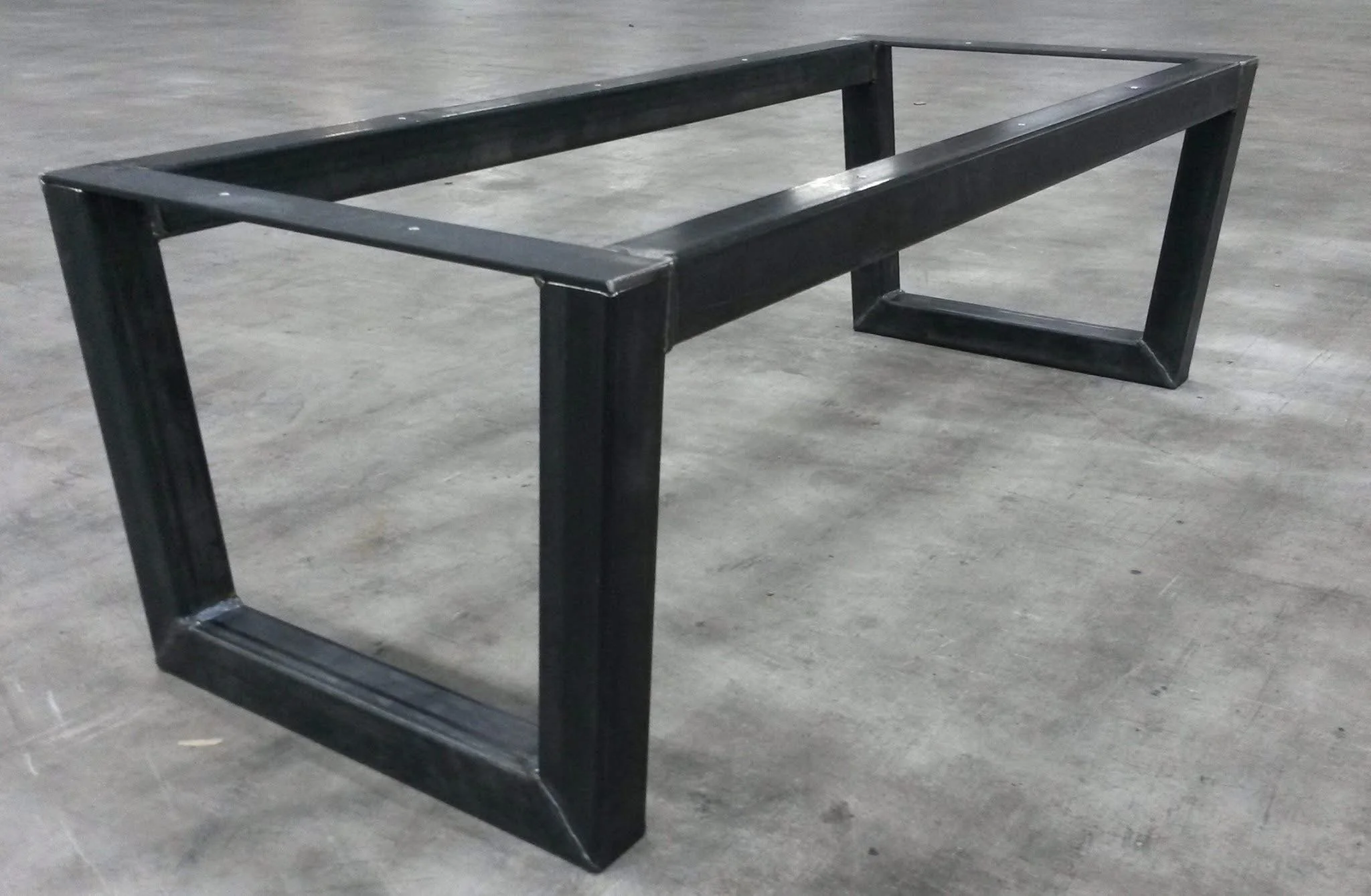 Een zwart metalen tafel zonder tafelblad, geplaatst op een betonnen vloer.