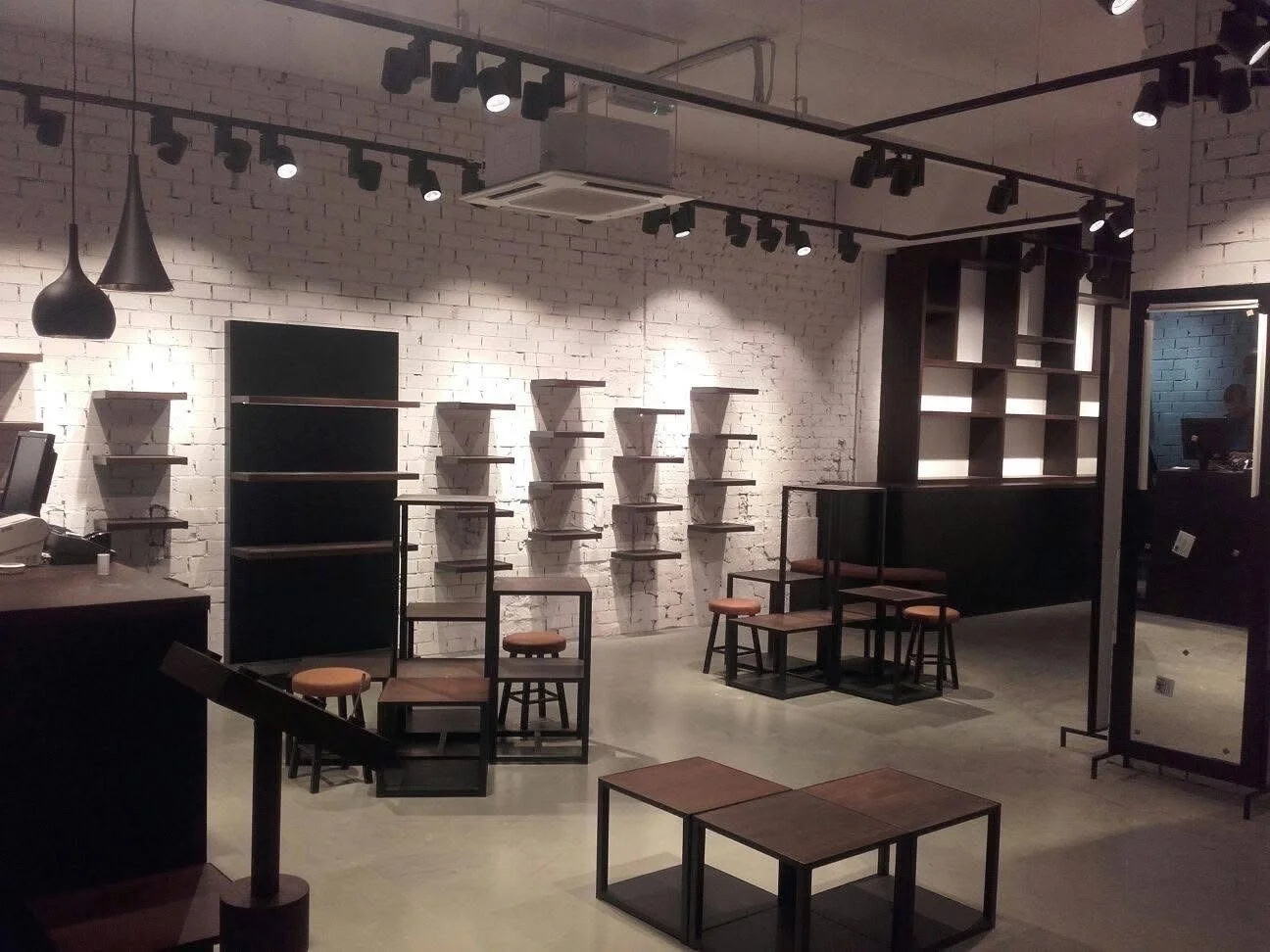 Leeg interieur van een moderne winkel of café met witte bakstenen muren, zwarte planken, stoelen en een spiegel.