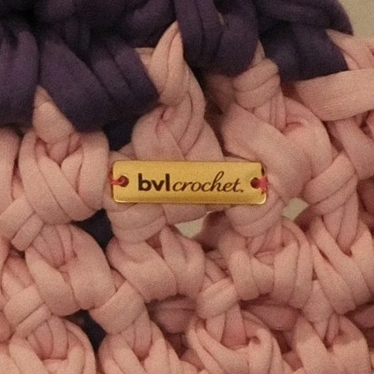 Close-up of a pink and purple chunky crochet blanket with a yellow tag that says "bvl crochet".