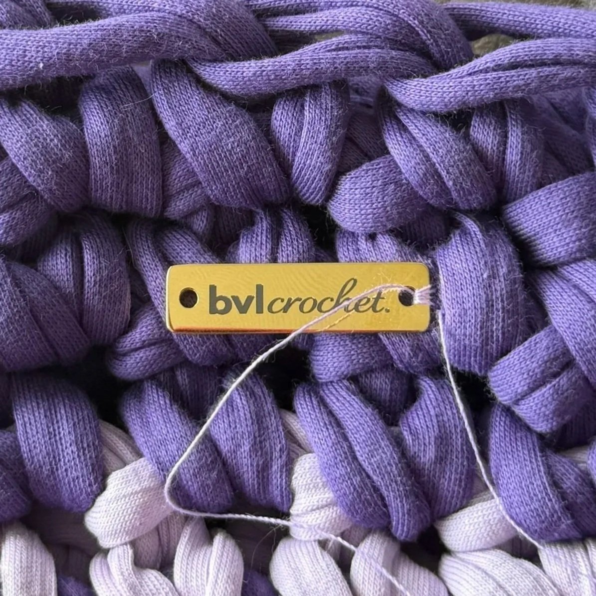 Close-up of purple and light purple yarn with a yellow tag labeled 'bvlcrocket' attached with a white string.
