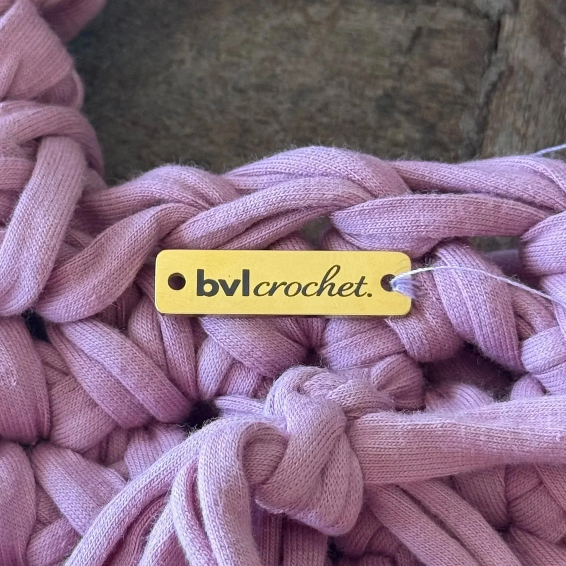 Close-up of a pink, twisted, fabric yarn with a yellow tag reading 'by crochet' attached.