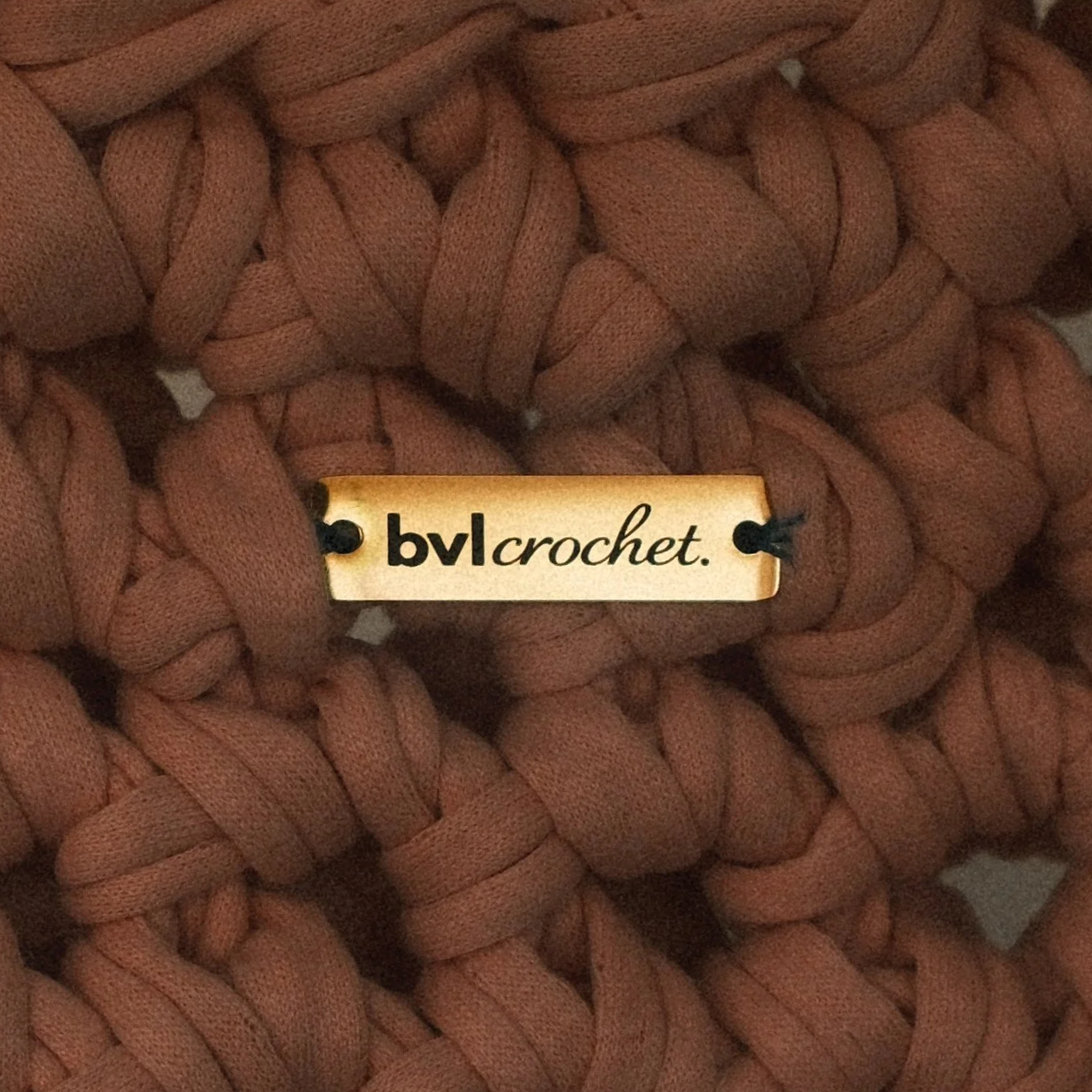Close-up of rust-colored, chunky, woven yarn with a small cream-colored label that reads 'bvl crochet' in black text.