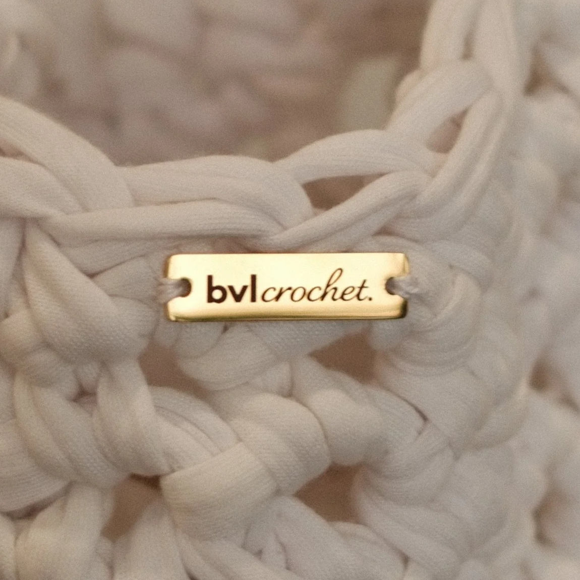 Close-up of white crocheted fabric with a metal tag that reads 'bvl crochet' attached to it.