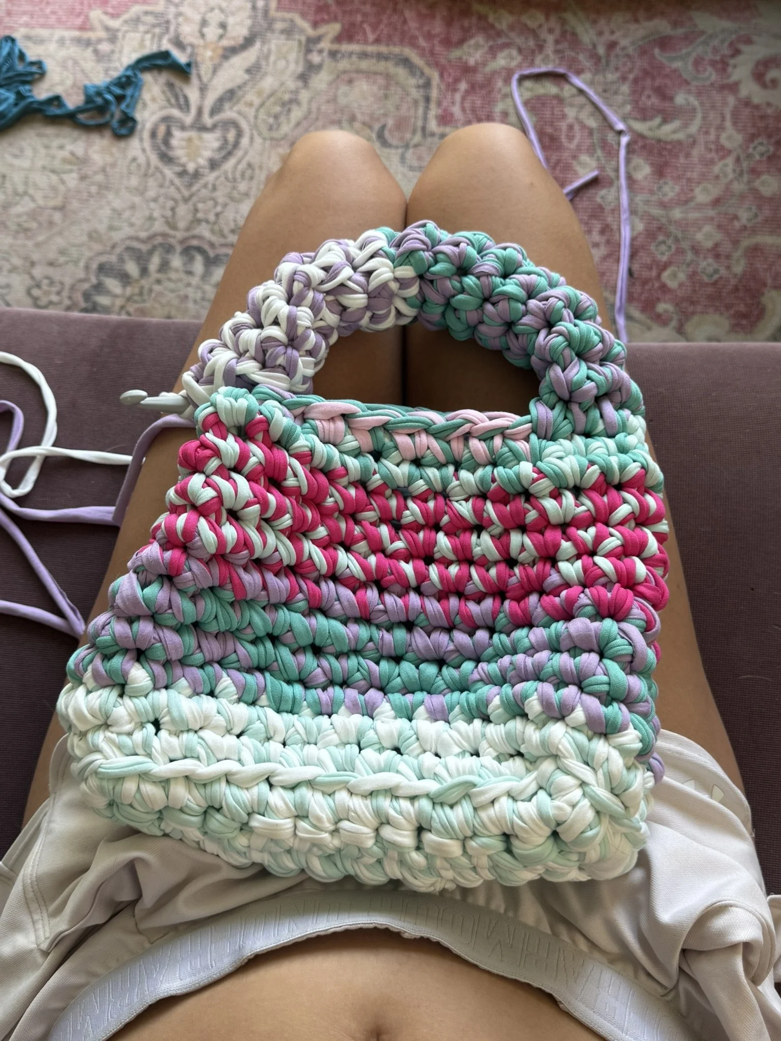 Colorful handmade crocheted bags in pastel colors resting on a person's lap indoors.