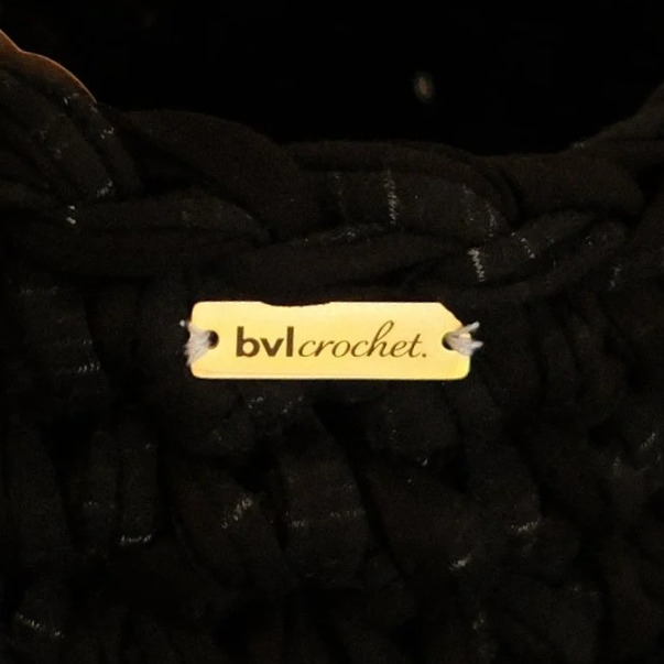 Close-up of a black knitted item with a yellow tag that has the text 'bvl crochet.'