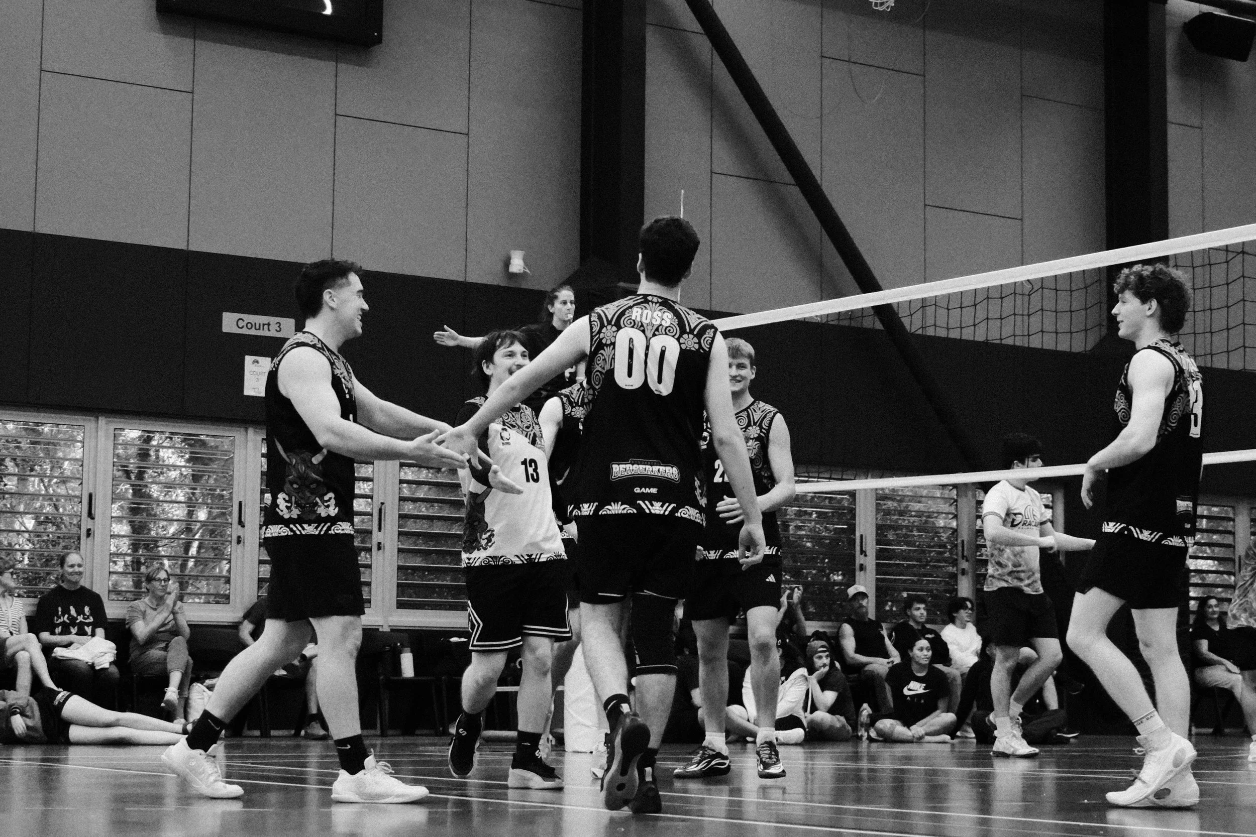 A group of volleyball players in team uniforms celebrating and shaking hands after a match in an indoor gymnasium.