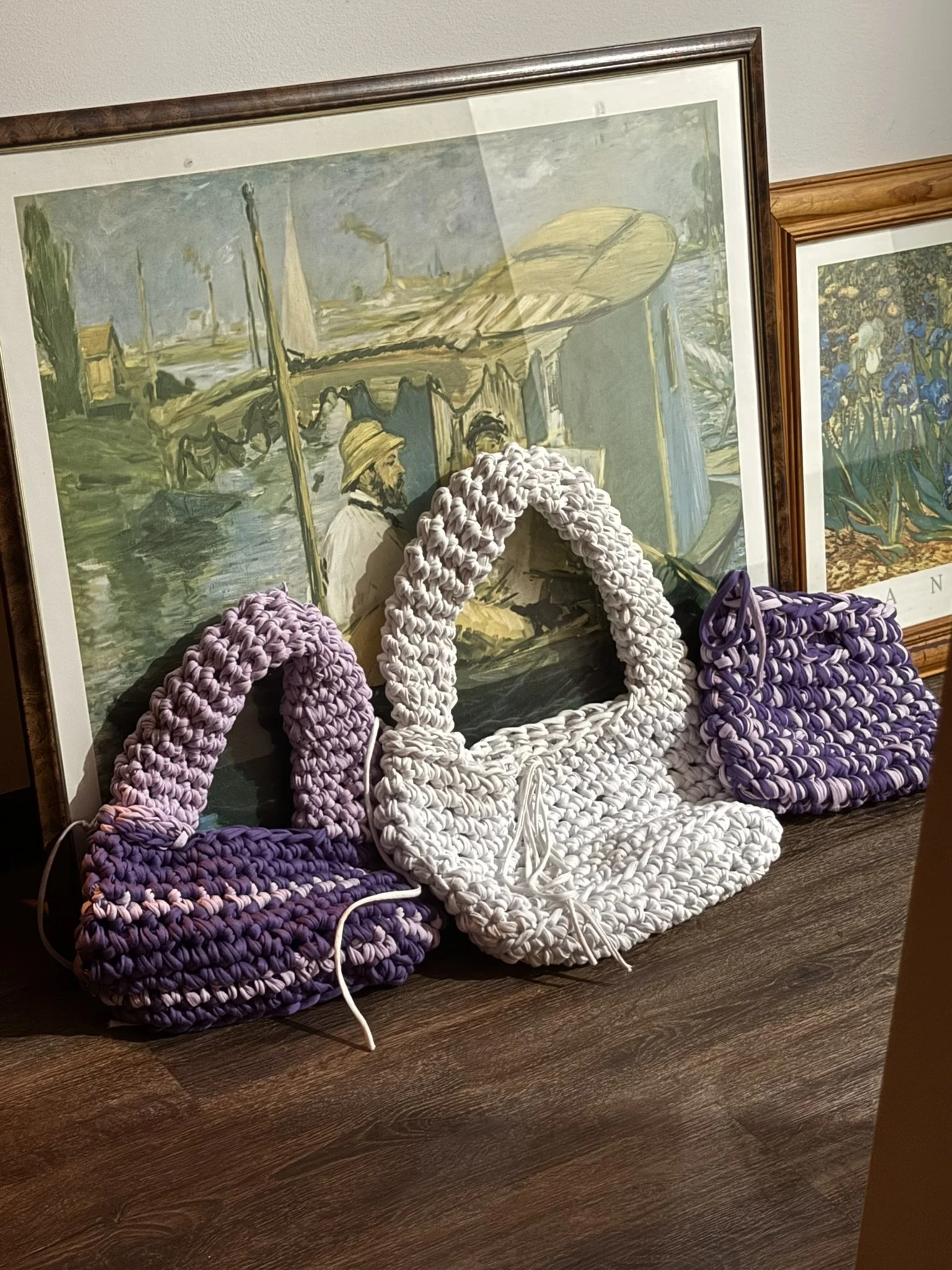 Cards and crochet purses arranged in front of framed landscape art on a wooden surface.