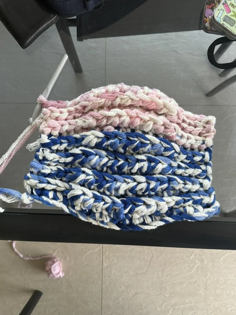 Two multicolored hand-knit scarves, one pink and one blue and white, draped over a black metal surface.