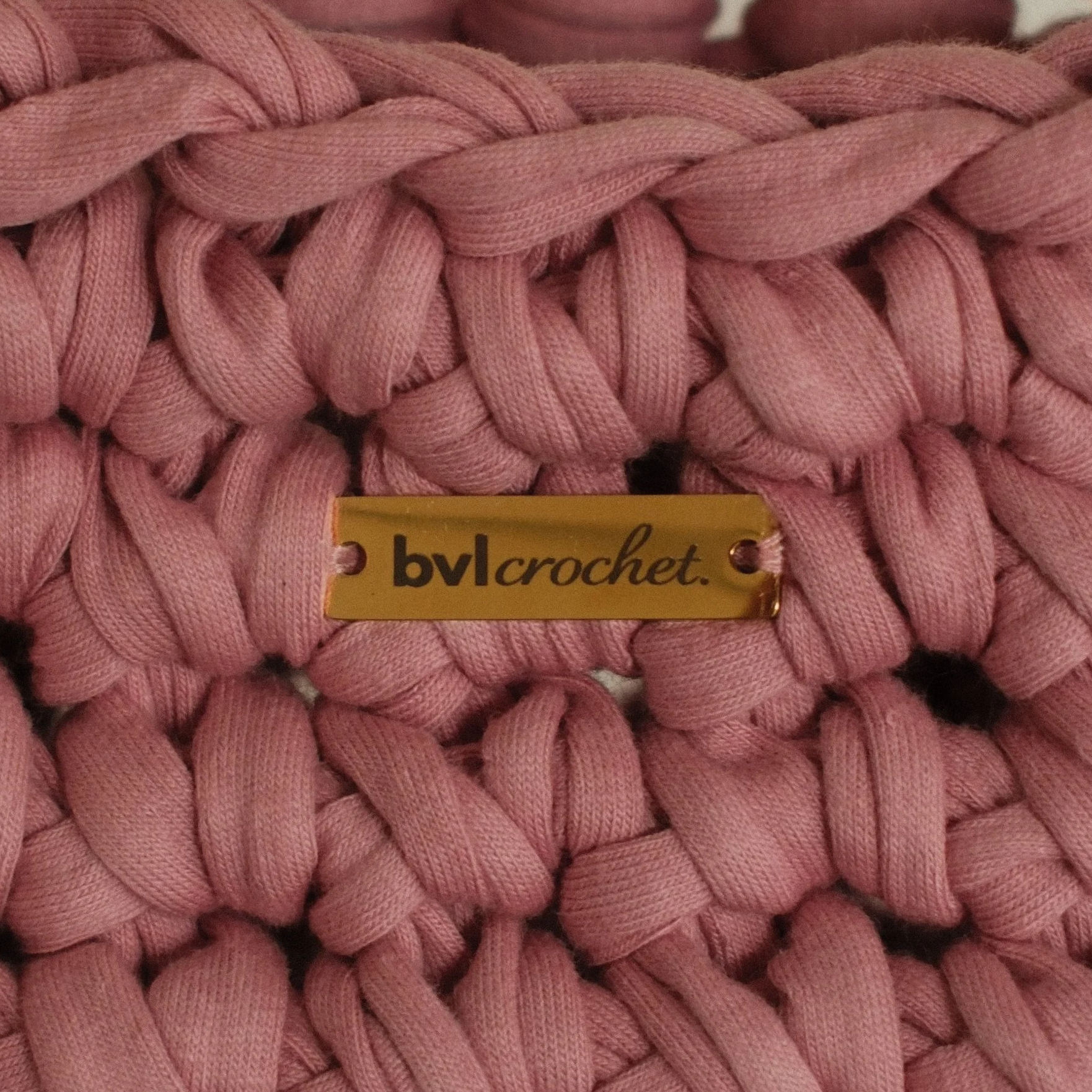 Close-up of pink twisted fabric strands with a yellow tag that has the word "bylcrochet" on it.