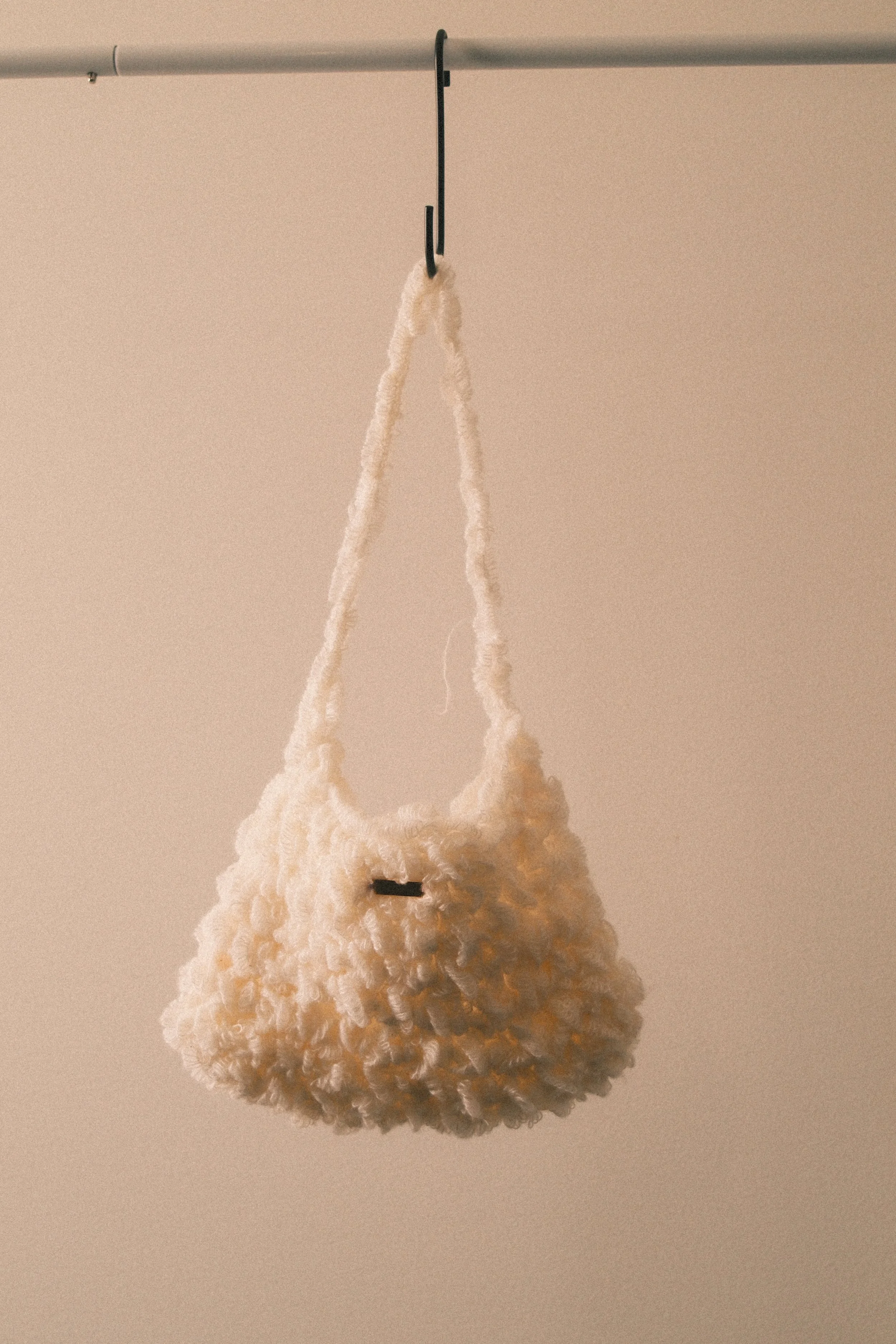 A beige pom-pom with a hanging loop attached to a black hook on a beige wall.