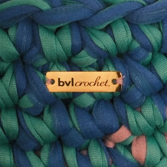 Close-up of a multicolored woven scarf with a small gold tag reading "bvl crochet."