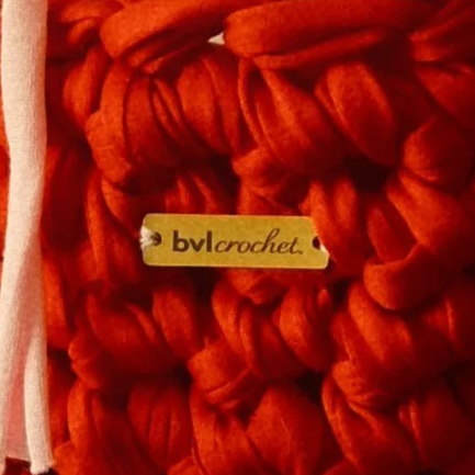 Close-up of chunky orange-red yarn with a BV crocket label.