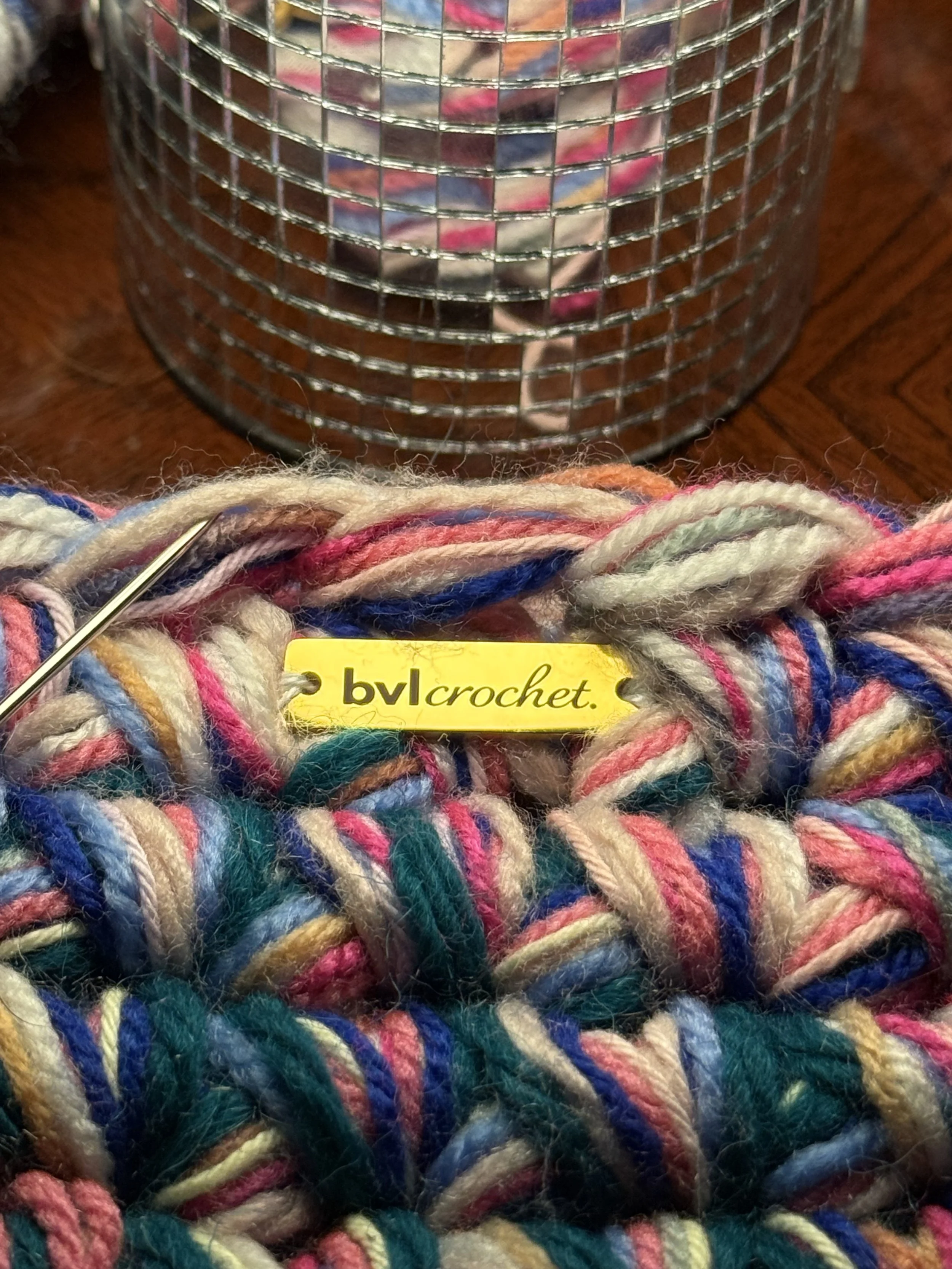 Close-up of multicolored yarn with a crochet hook, and a knitting supply container in the background.