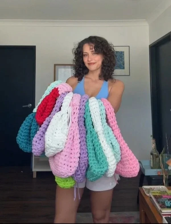 A woman holding multiple colorful crocheted blankets in a room with modern decor.