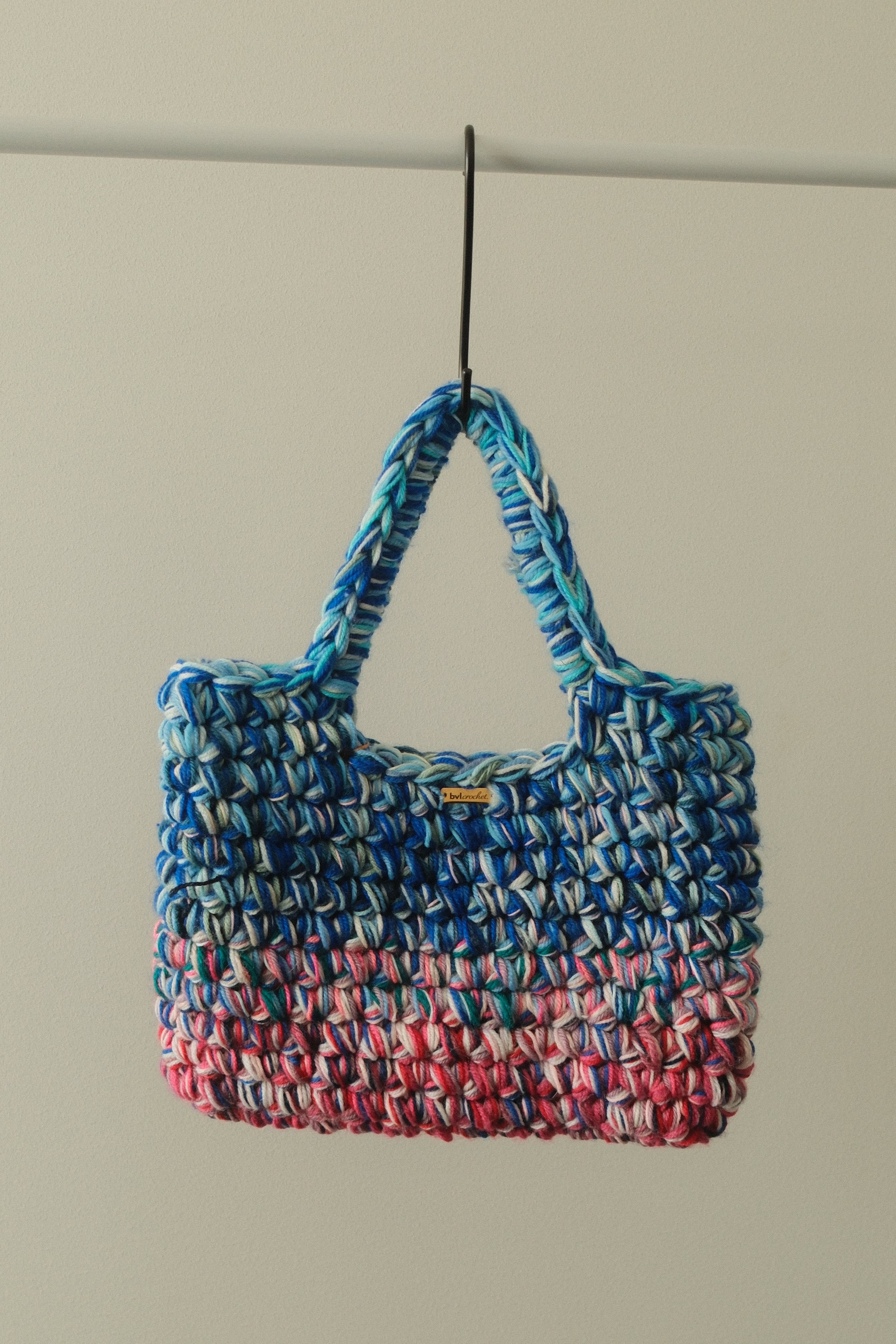 Colorful woven tote bag hanging from a hook on a ceiling.