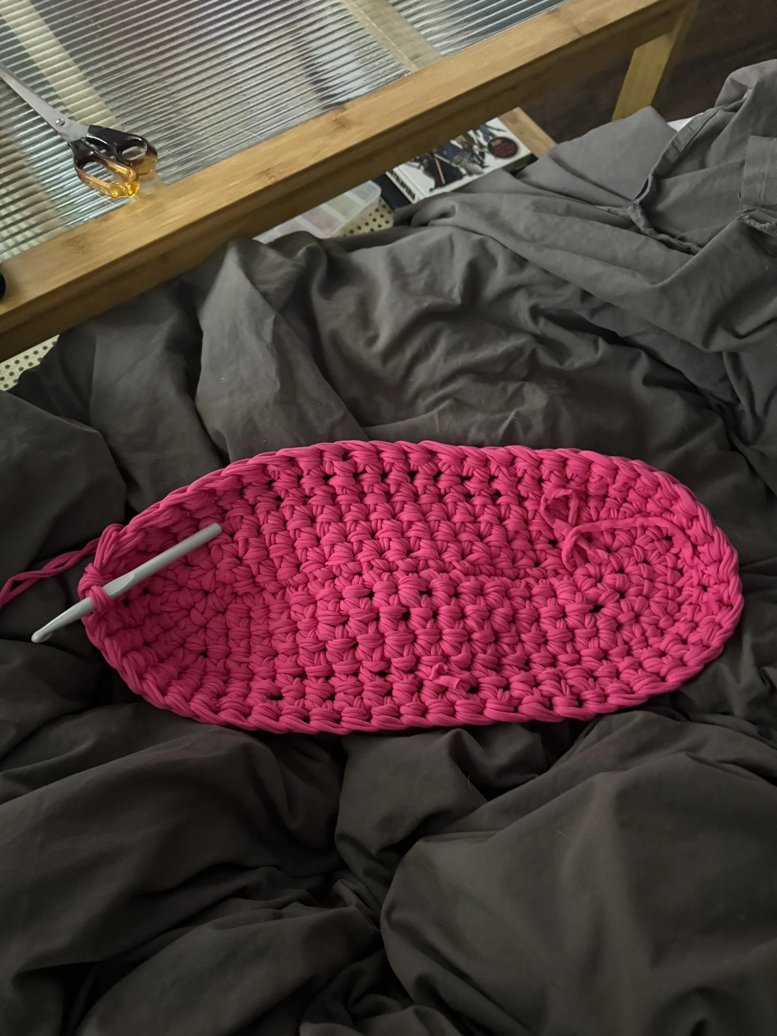 Pink crochet basket placed on dark gray fabric with a white pen inside it, and a pair of scissors on a wooden surface in the background.