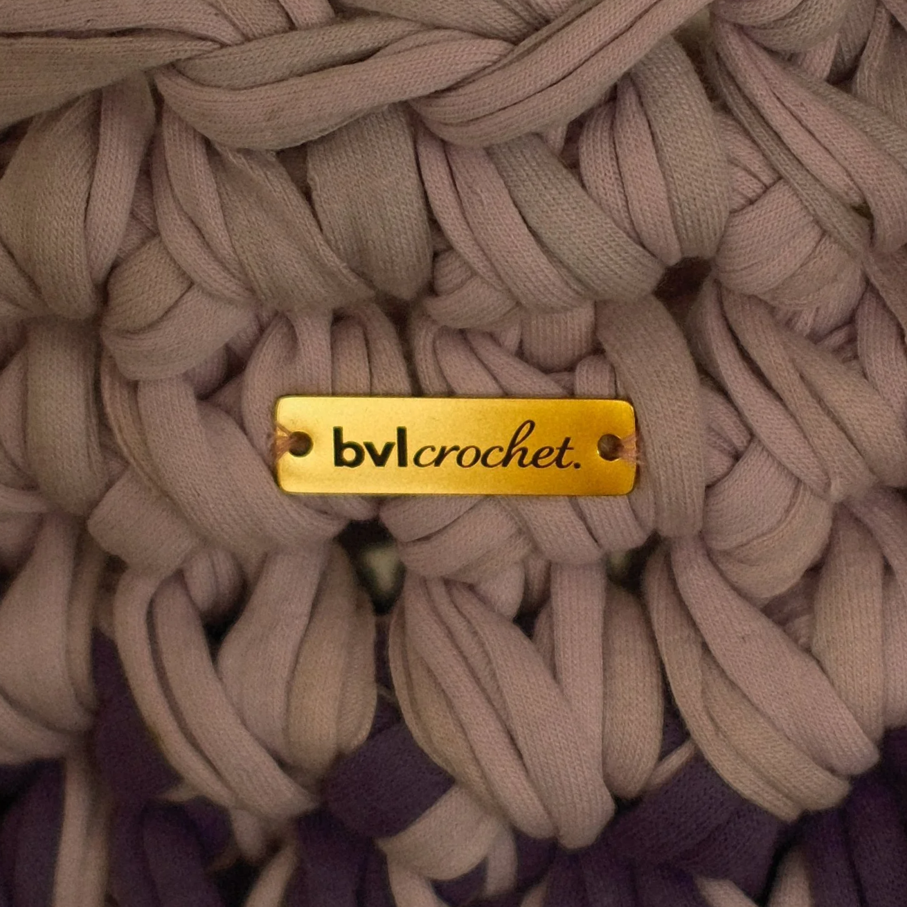 Close-up of a beige, chunky knit fabric with a gold metallic tag that reads 'bv crocket' attached to the fabric.