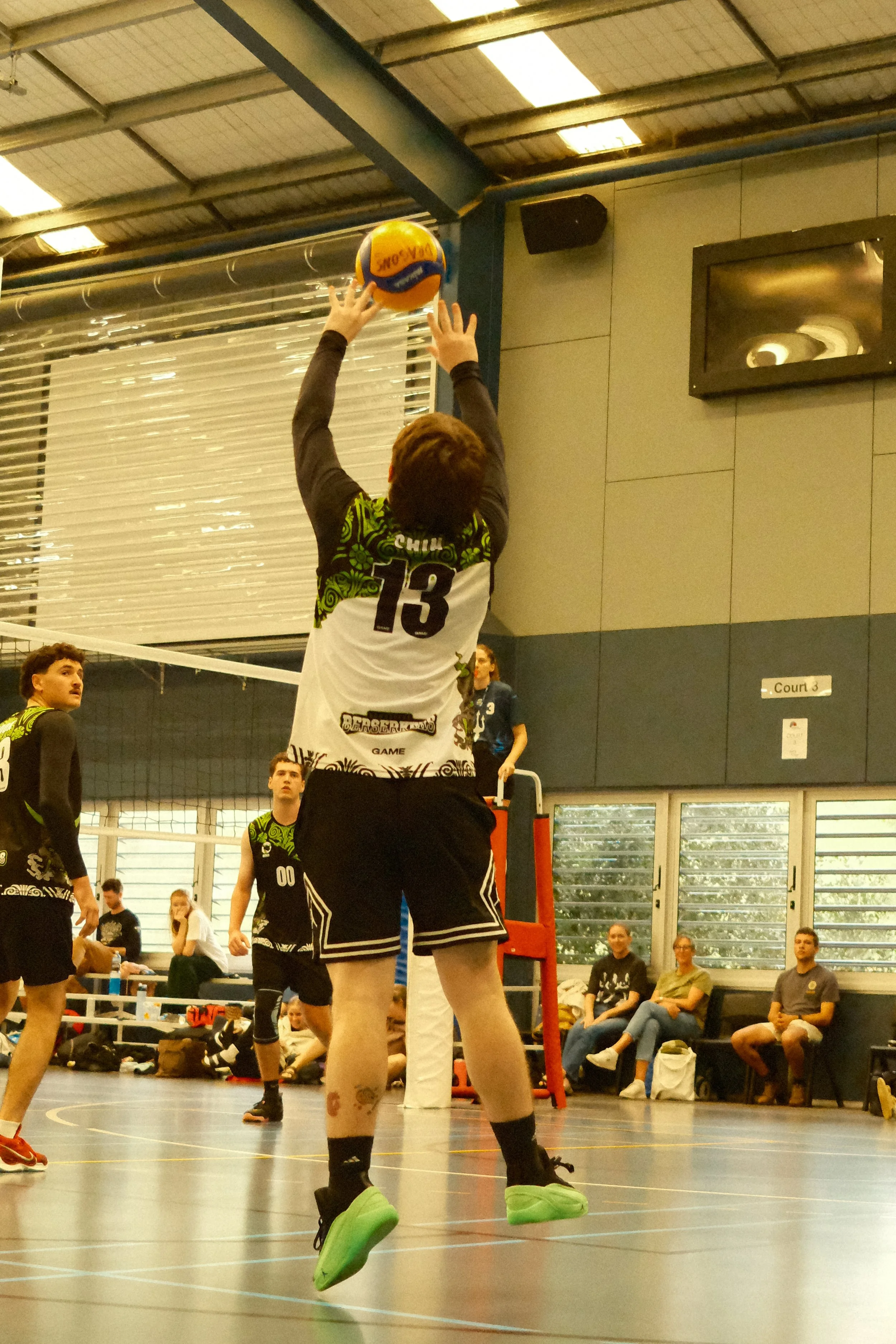 A volleyball player leaping in the air to hit the ball during an indoor volleyball game, with spectators watching from the sidelines.