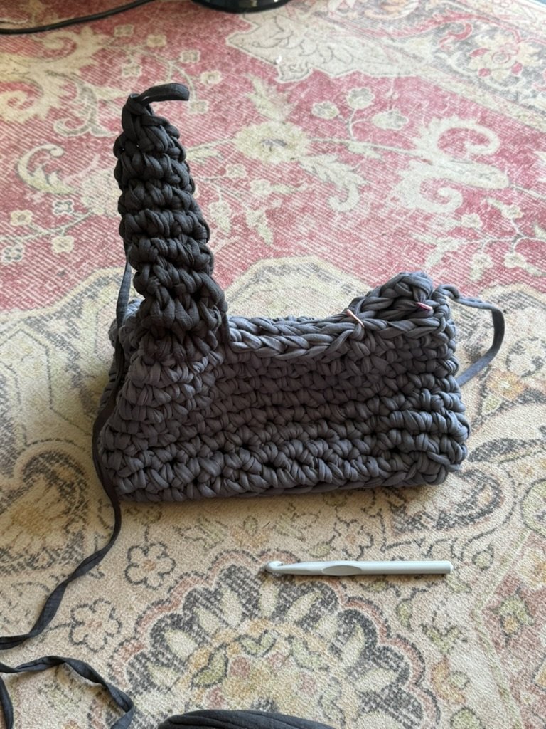 Gray, chunky crochet bag on a patterned rug with a white pen underneath.