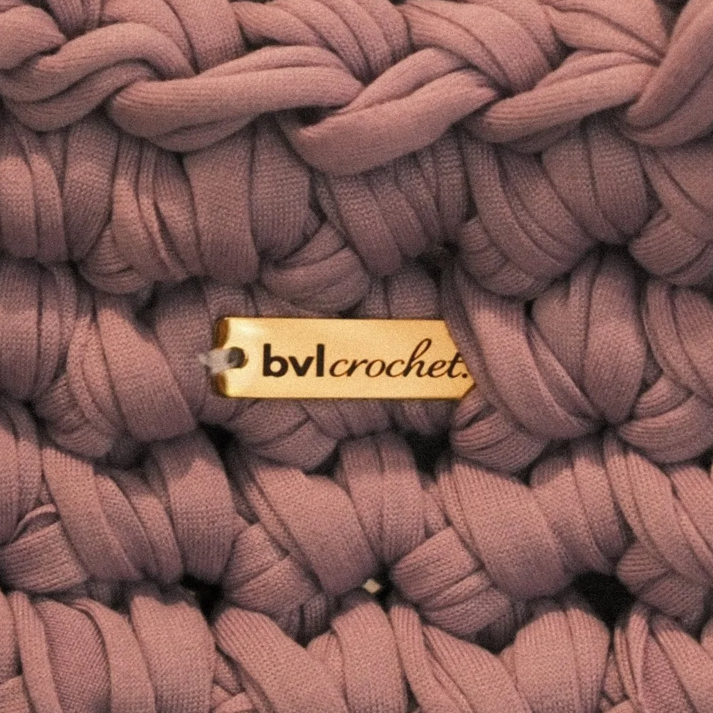 Close-up of mauve chunky knit yarn with a gold tag reading 'bvlcrochet.'