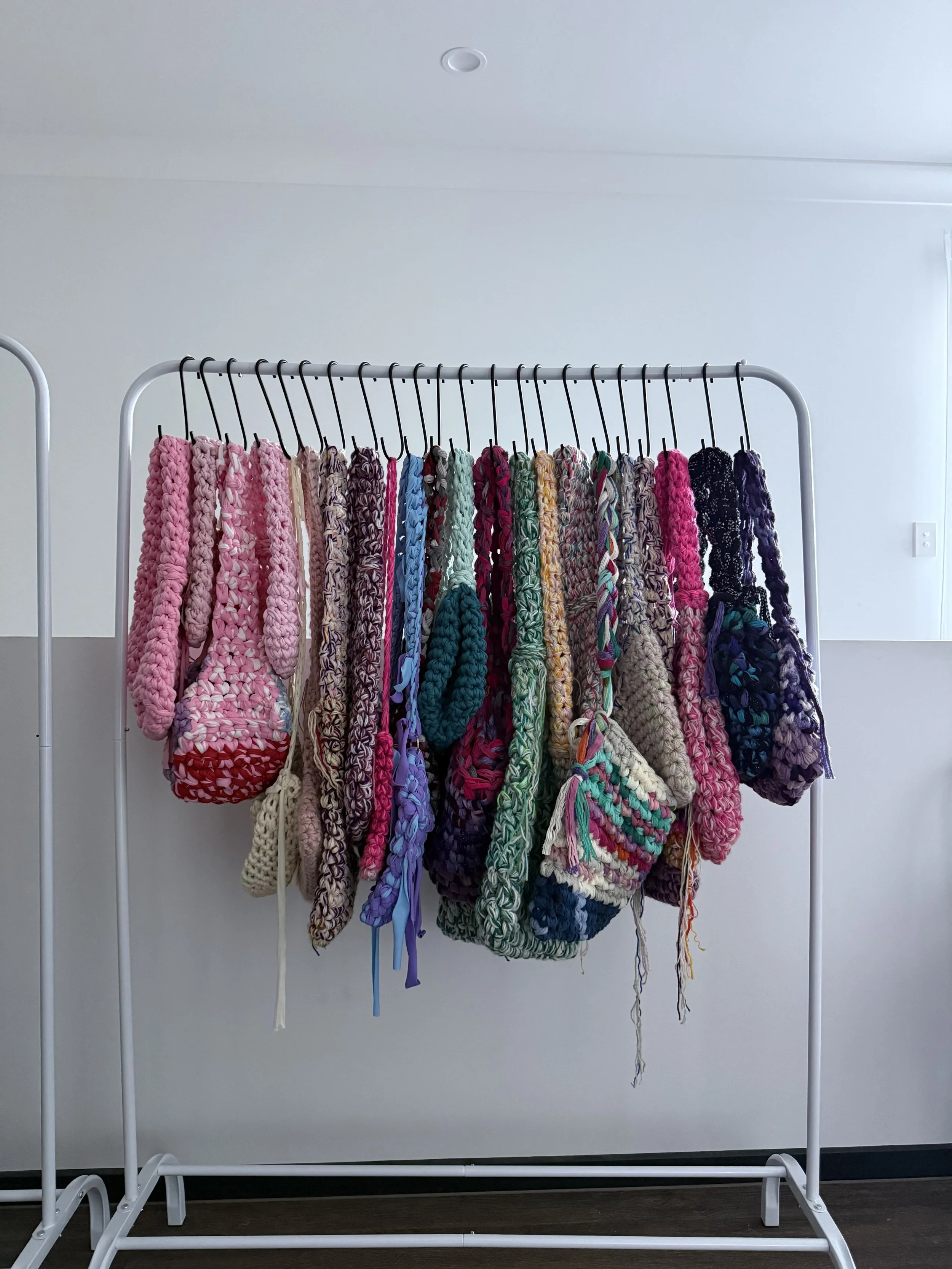 A metal clothing rack with multiple hand-knit scarves in various colors and patterns hanging from black hooks.