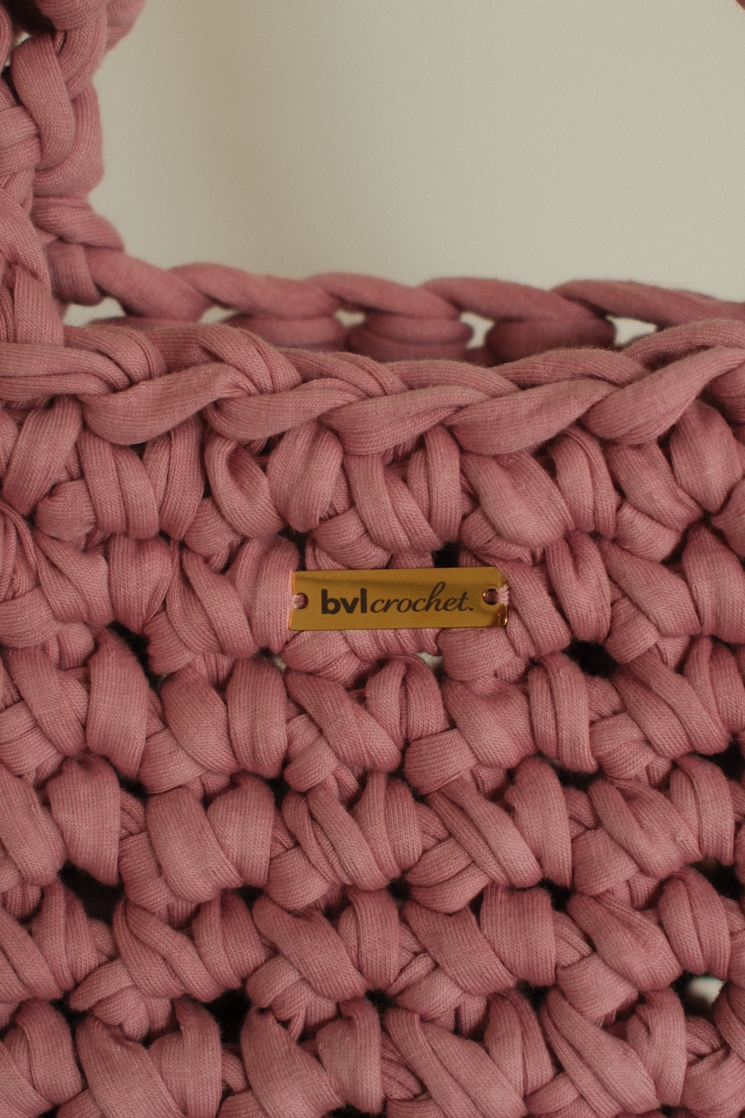 Close-up of pink rope crocheted into a basket with a gold label reading 'by crochet'.
